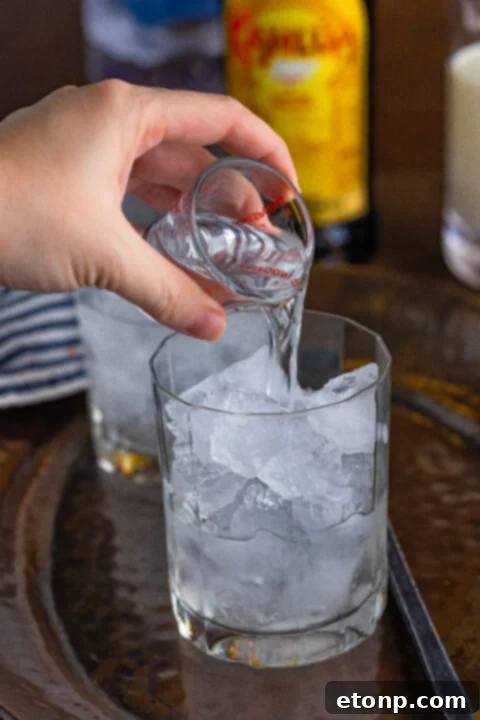 Close-up of a White Russian being mixed in a glass, with ice and liquids combining.