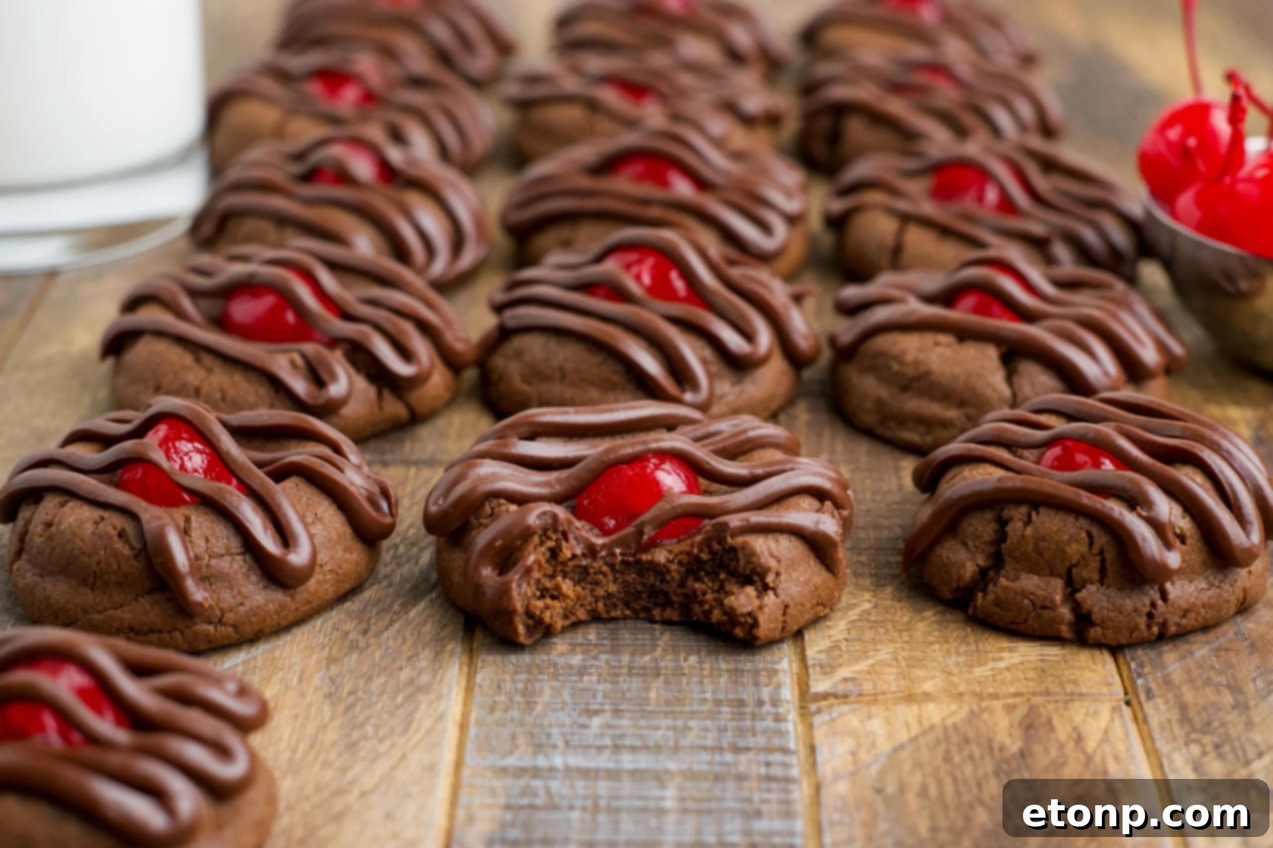 Delicious homemade Chocolate Cherry Cookies arranged on a rustic wooden table, with one cookie artfully bitten to reveal its soft, chocolatey interior and a vibrant, juicy maraschino cherry at its heart.