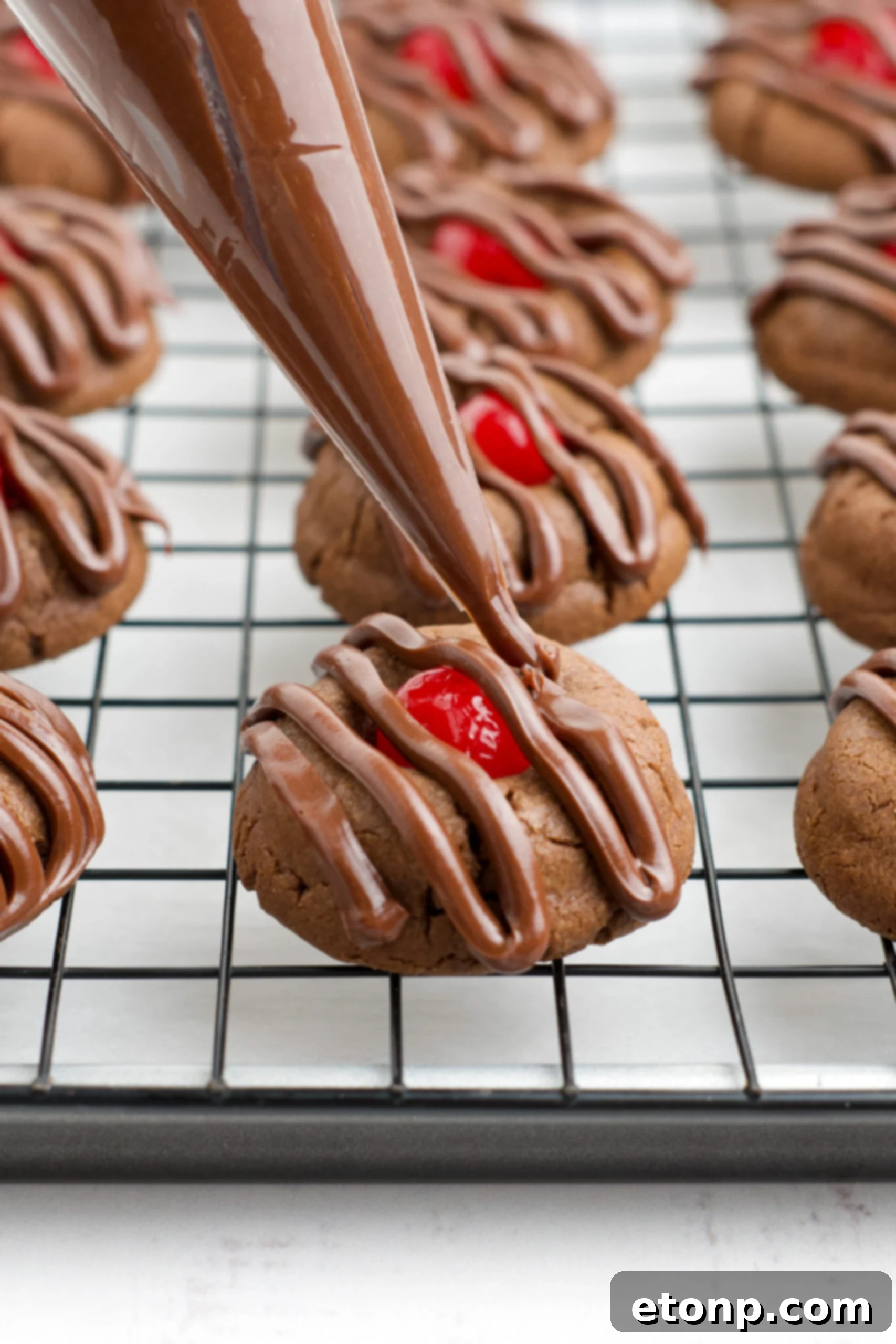 A close-up shot of a piping bag expertly applying a smooth, glossy chocolate cherry frosting onto a freshly baked cookie, creating an elegant and irresistible finish.