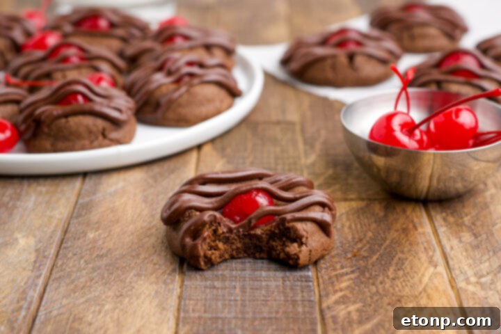 A close-up of a delightful Chocolate Cherry Cookie on a wooden table, featuring a missing bite that reveals its tempting, soft interior and the juicy cherry center.