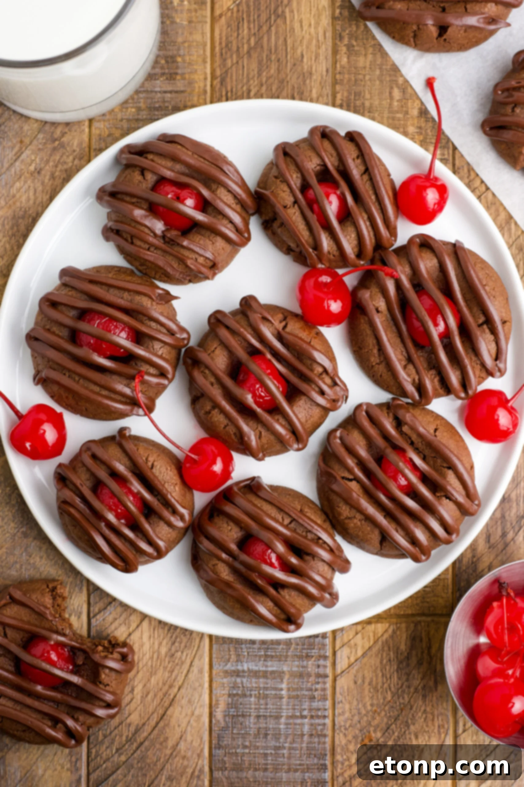 Overhead view of a white plate generously filled with perfect Chocolate Cherry Cookies, artfully placed with fresh maraschino cherries scattered around, creating an inviting and colorful display.