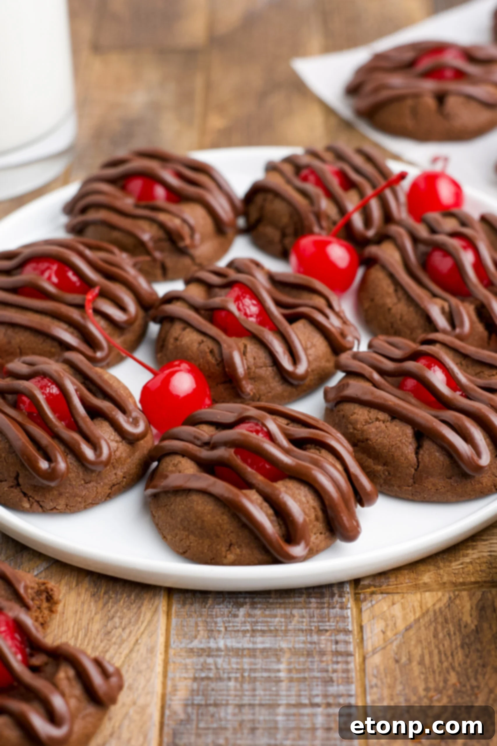 A close-up of decadent Chocolate Cherry Cookies on a white plate, with a decorative scattering of vibrant maraschino cherries nearby, inviting you to enjoy this delightful treat.