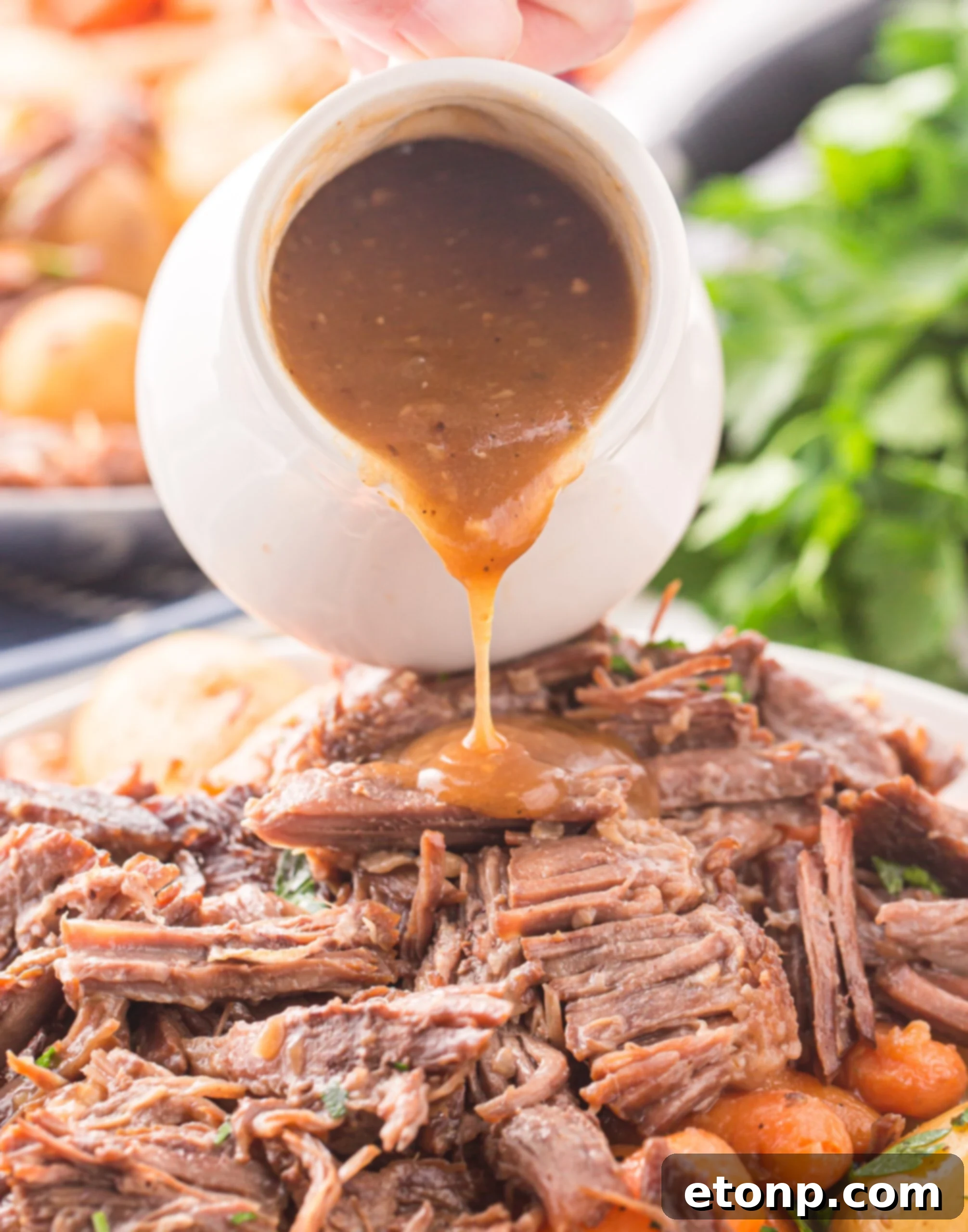 Pouring gravy from a white gravy boat onto the pot roast. 
