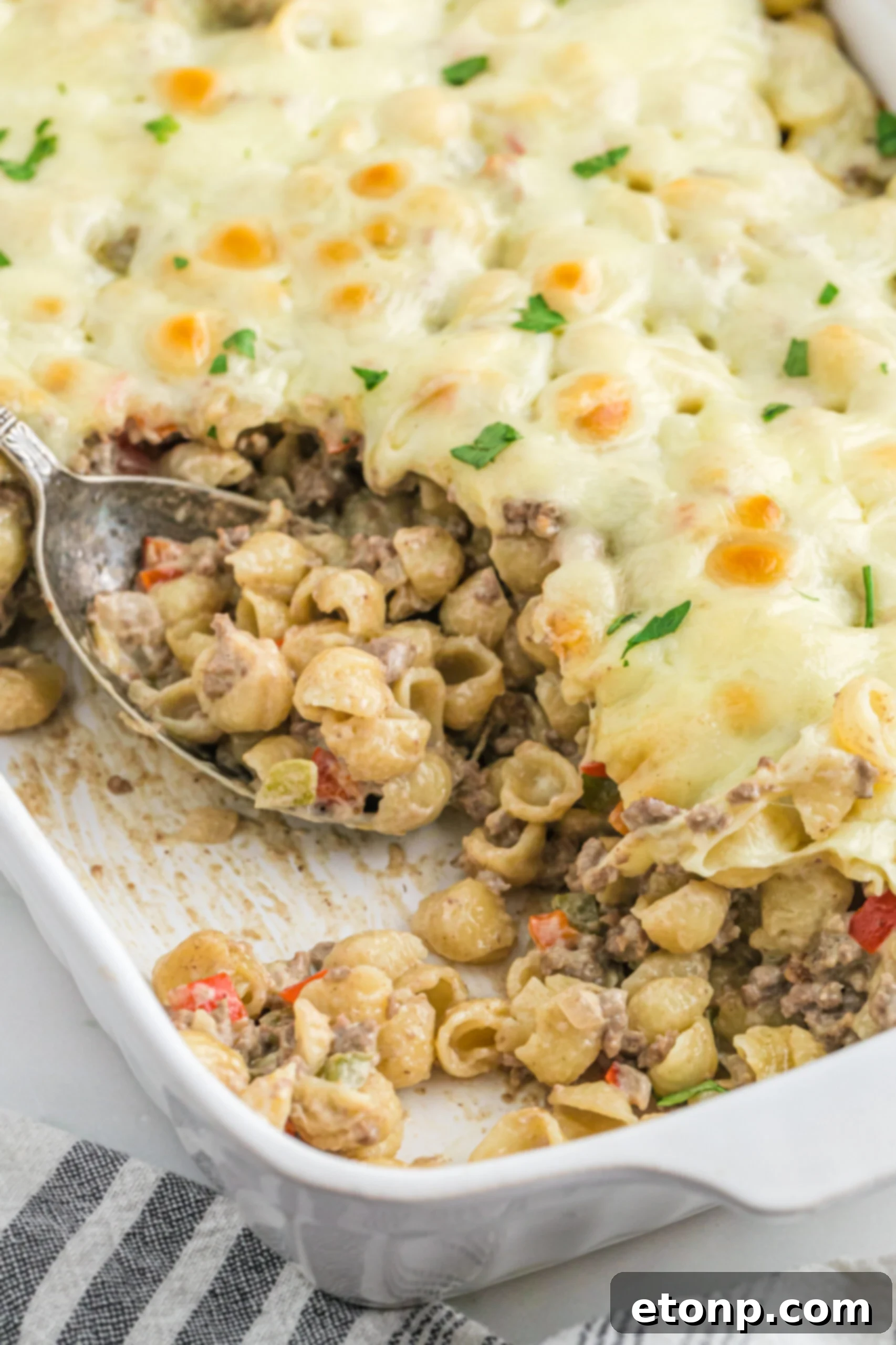 Front view of Philly Cheesesteak Casserole in a white baking dish with a silver spoon.