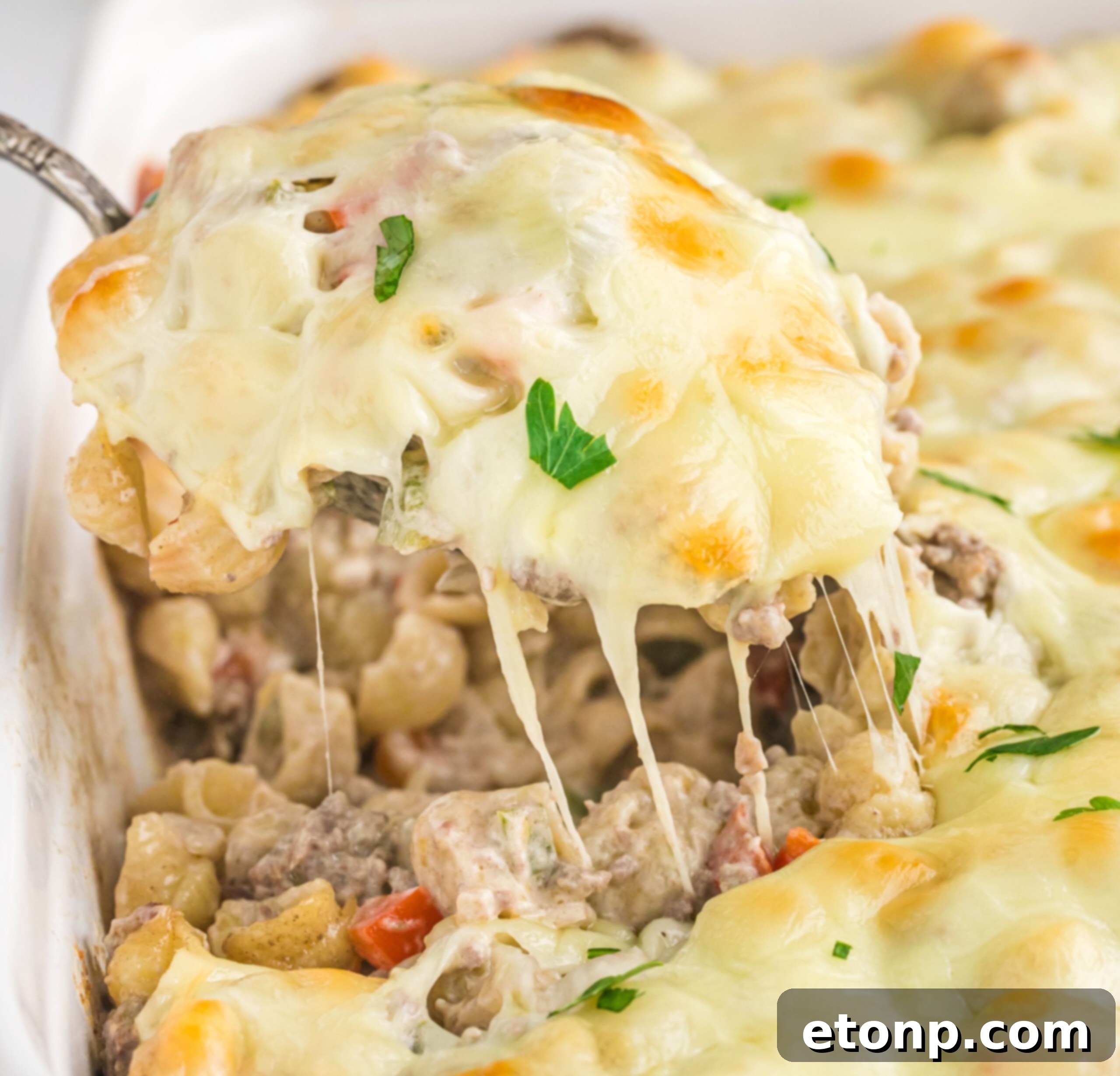Front view of Philly Cheesesteak Casserole in a white baking dish with a silver spoon removing a spoon full.
