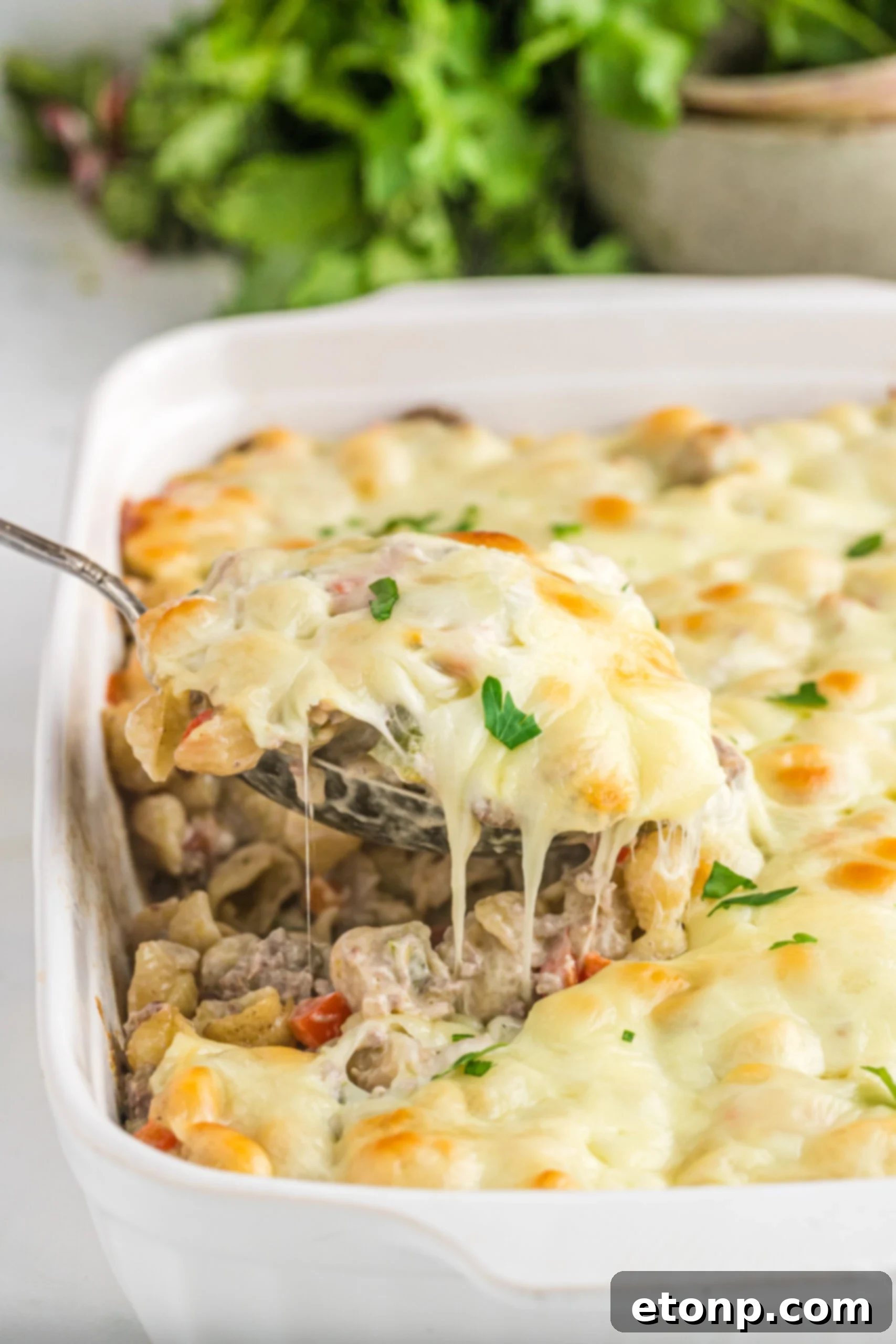 Front view of Philly Cheesesteak Casserole in a white baking dish with a silver spoon removing a spoon full.