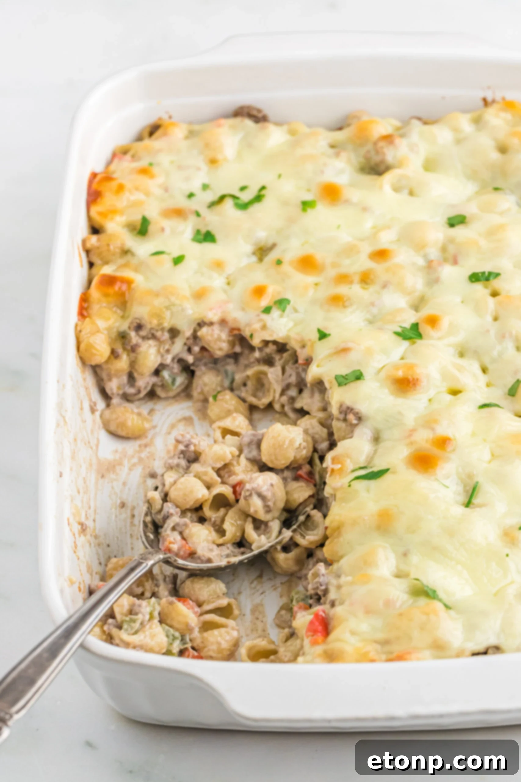 Front view of Philly Cheesesteak Casserole in a white baking dish with a silver spoon.