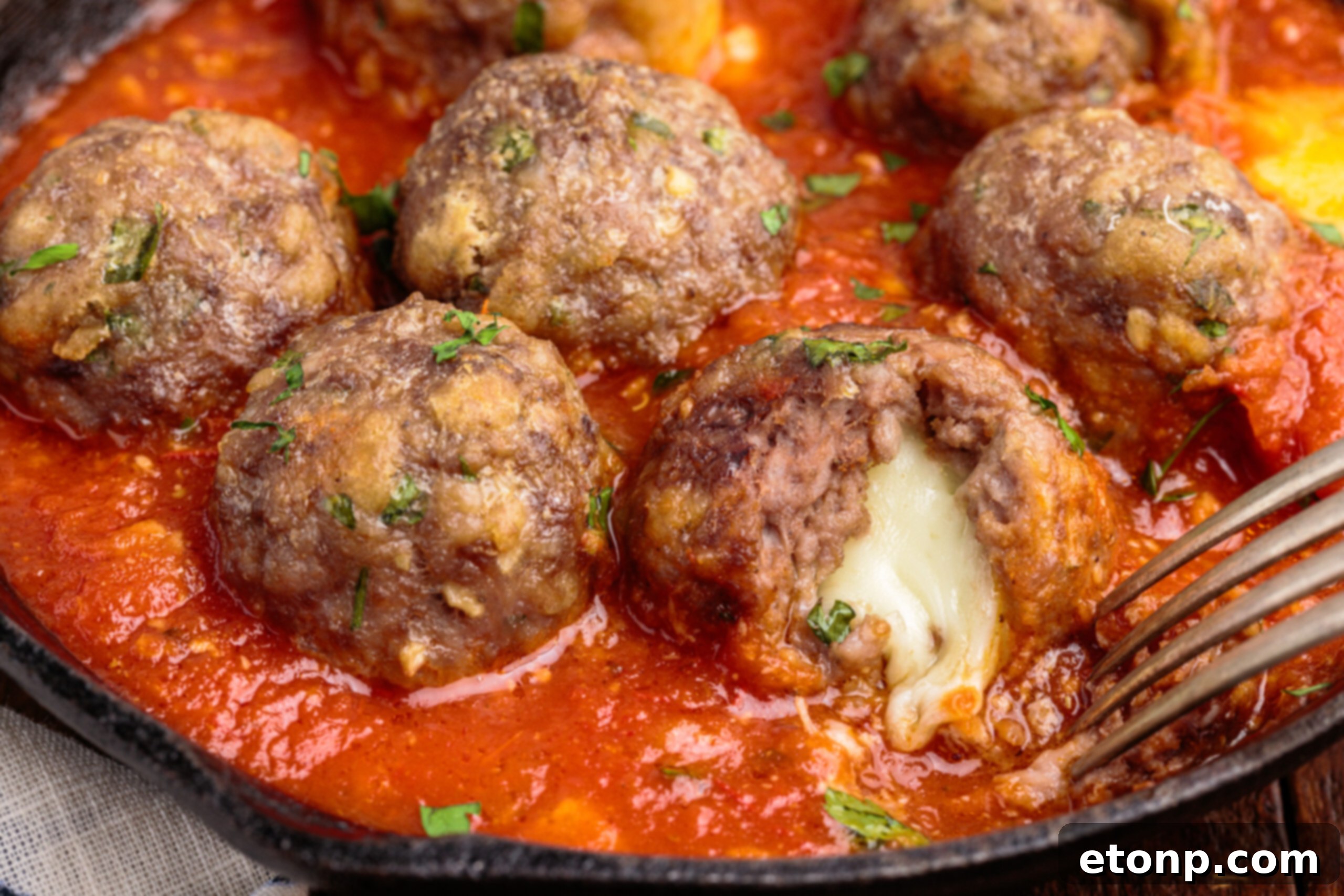 Gooey Mozzarella Meatballs 16 Up close view of a Mozzarella Stuffed Meatball, cut to reveal the hot, melted cheese, on a fork in a cast iron skillet.