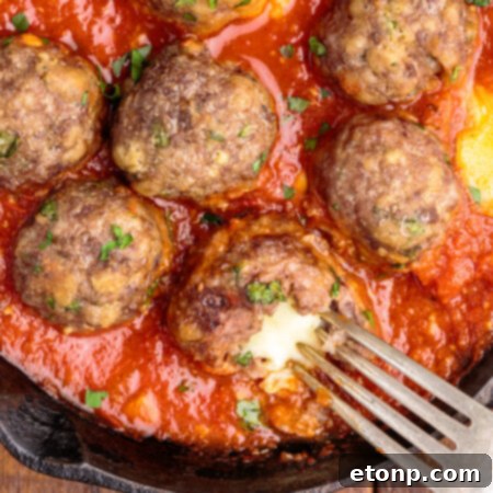 Gooey Mozzarella Meatballs 17 Overhead view of Mozzarella Stuffed Meatballs in a cast iron skillet with one meatball cut open by a silver fork, showcasing the melty mozzarella core.