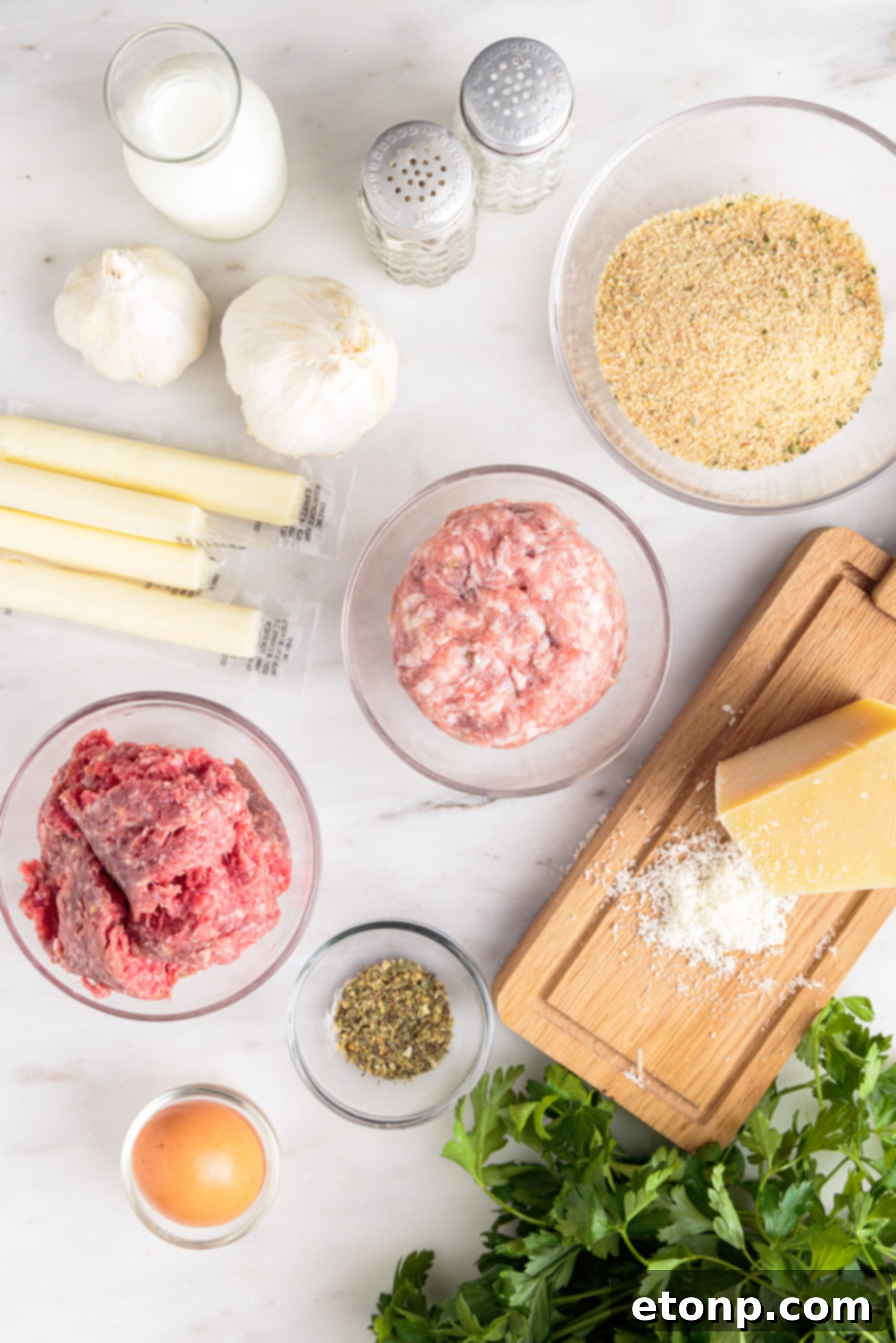 Gooey Mozzarella Meatballs 7 Overhead view of fresh ingredients for Mozzarella Stuffed Meatballs, including ground beef, pork, breadcrumbs, milk, egg, parsley, Parmigiano Reggiano, garlic, salt, pepper, and mozzarella cubes.