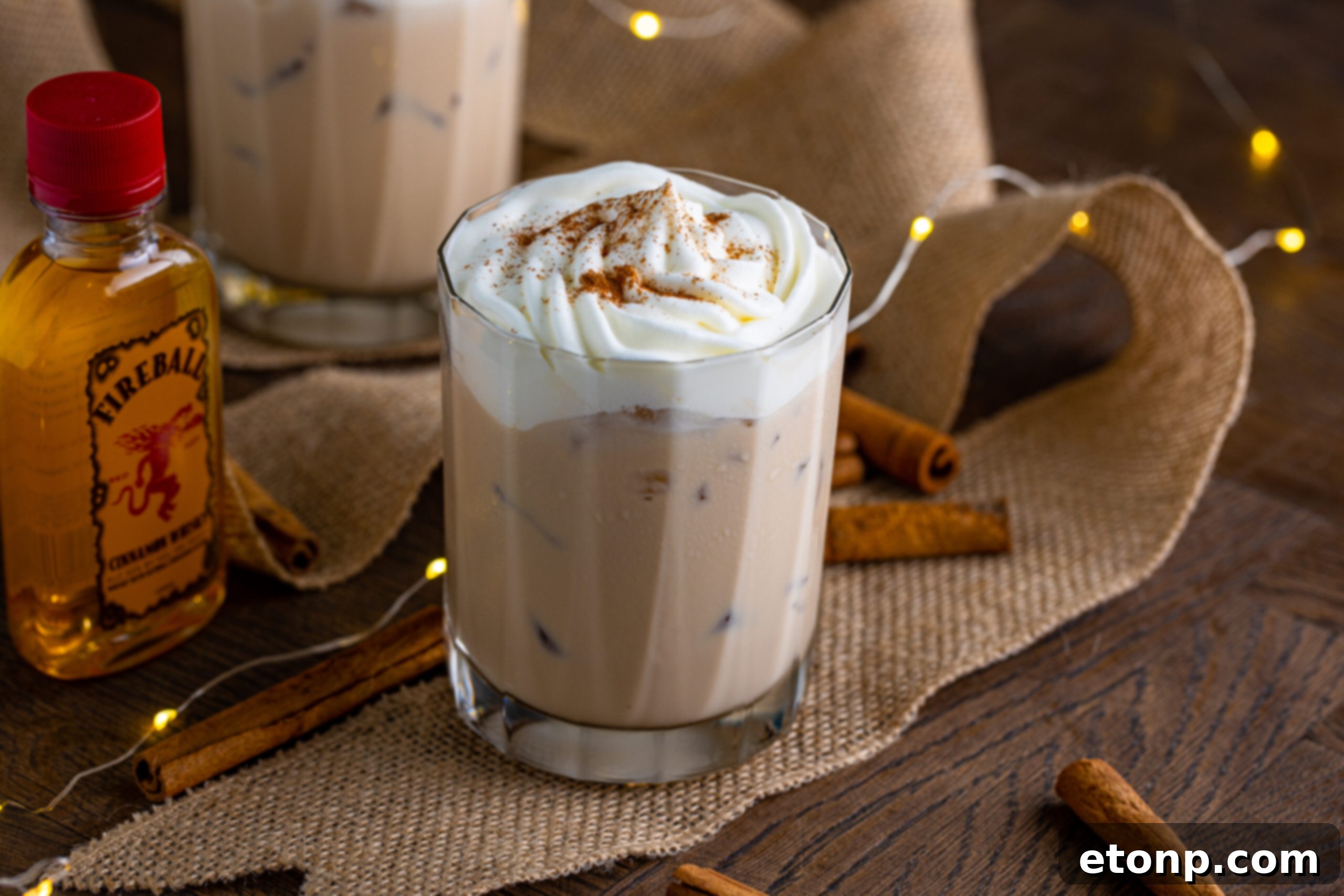 The cinnamon roll cocktail in a clear glass topped with whipped cream and dusted with cinnamon 