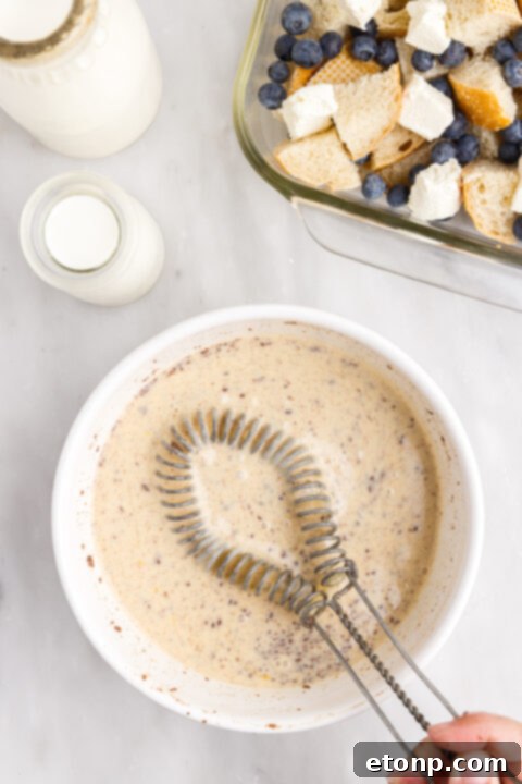 Egg, milk, and cream mixture being whisked in a large bowl.