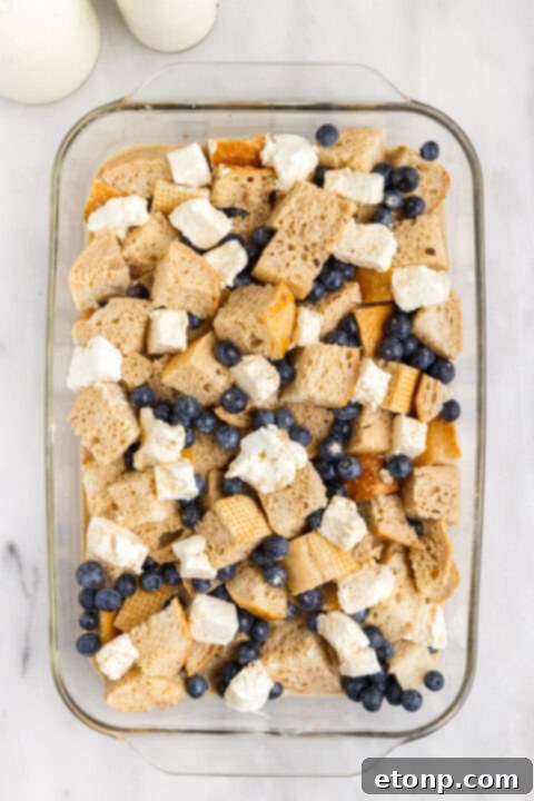 Custard mixture being poured evenly over the bread and berries in the baking dish.