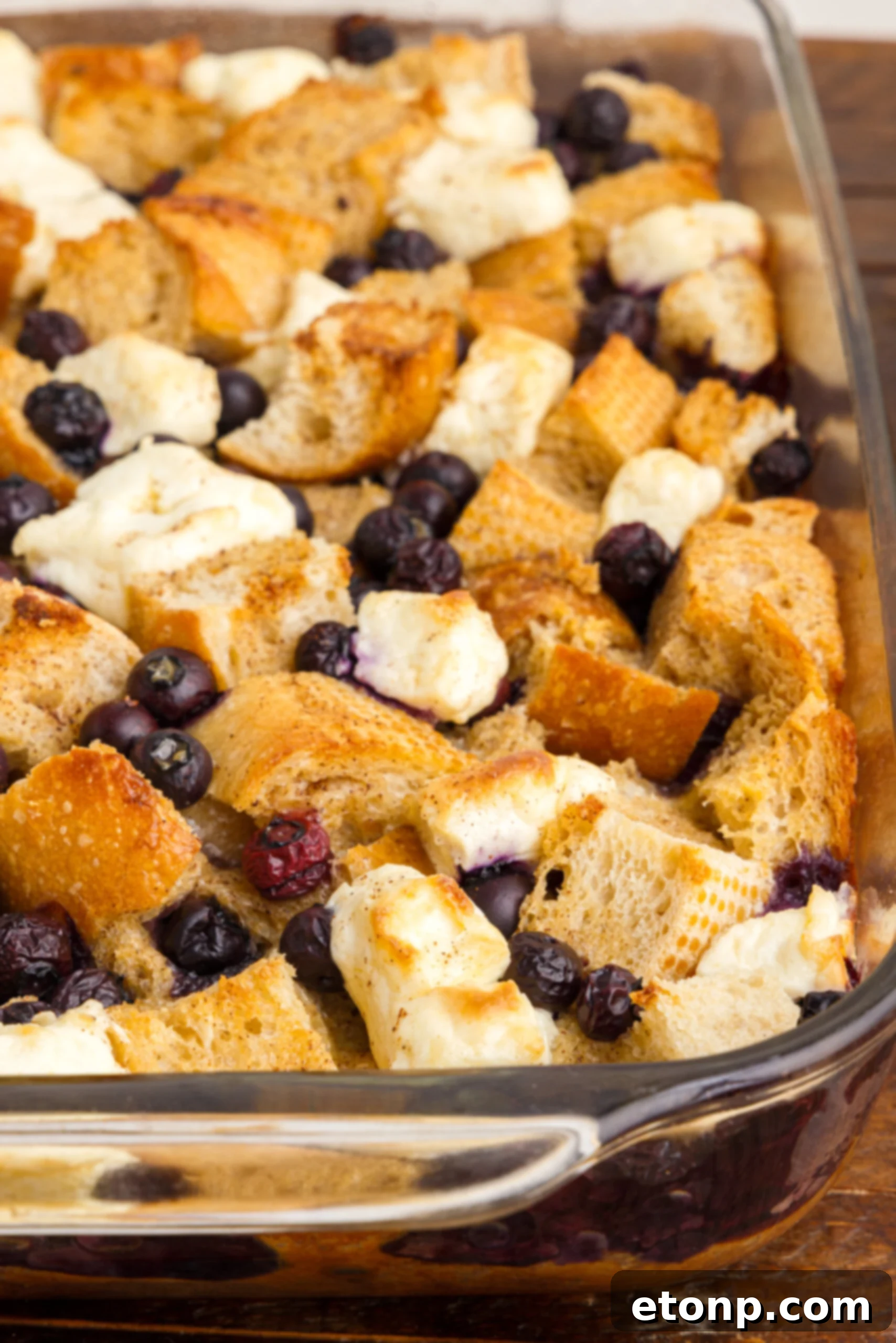 Close-up view of the rich, textured surface of Blueberry French Toast Casserole in a clear glass baking dish, showing the golden-brown crust and visible blueberries.