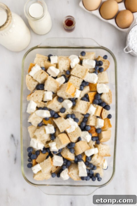 Blueberries being sprinkled over bread cubes in a baking dish.