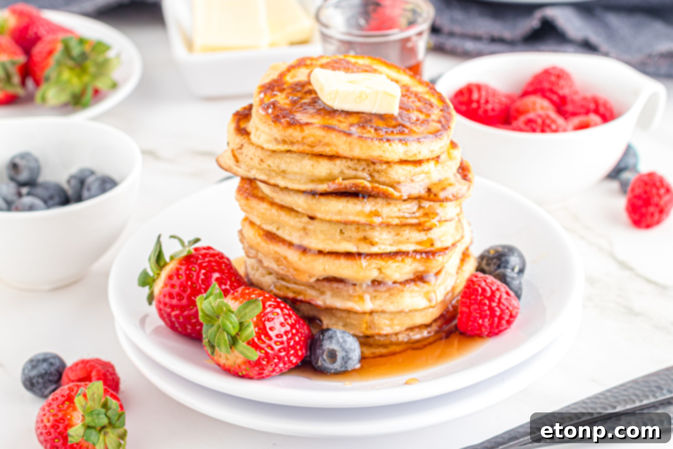 Mini Pancakes stacked on a white plate topped with syrup and butter 