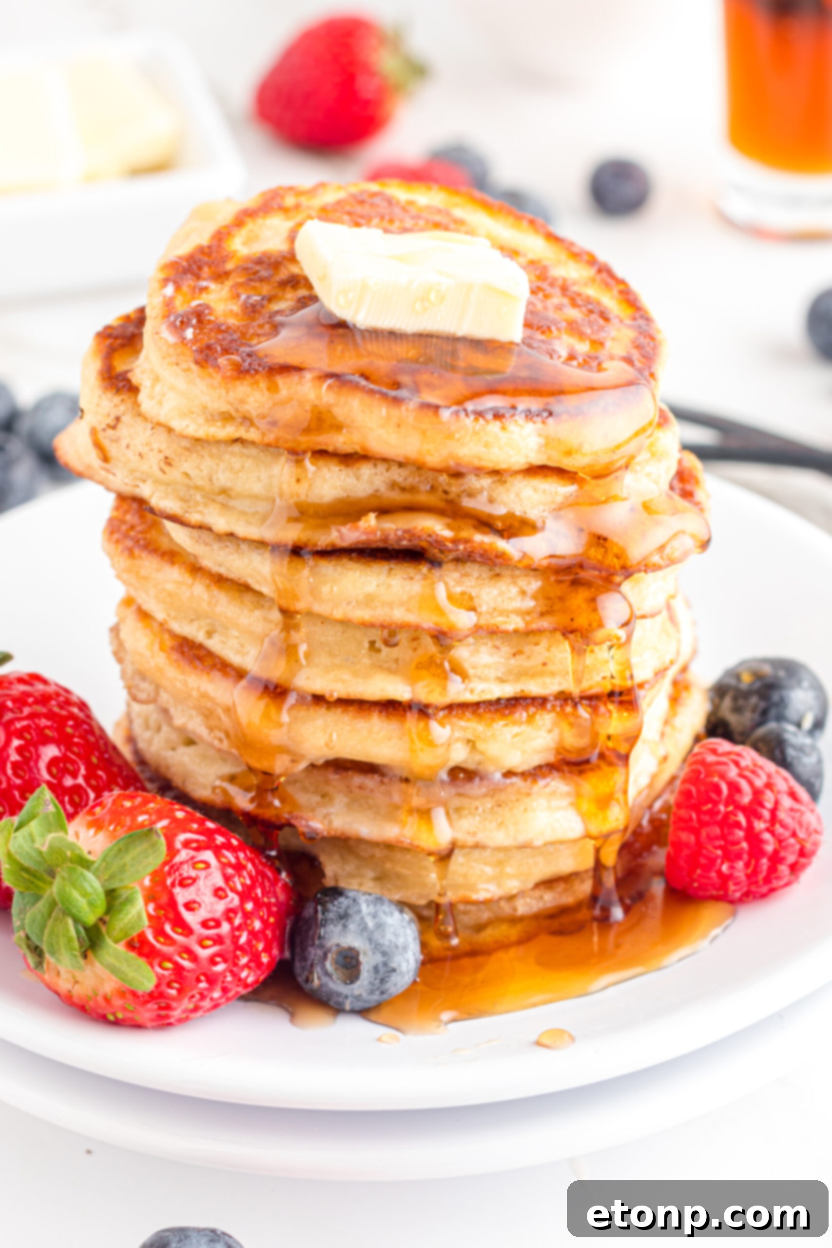 Close up shot of Mini Pancakes stacked on a white plate topped with syrup and butter 