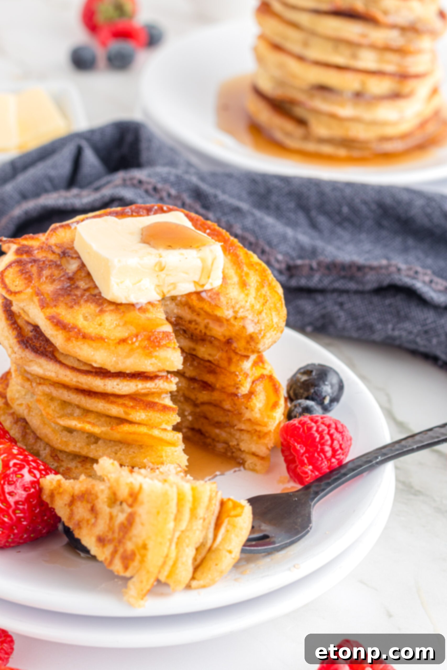 Front view of Mini Pancakes on a white dish served with strawberries and blueberries with a bite removed from a silver fork.