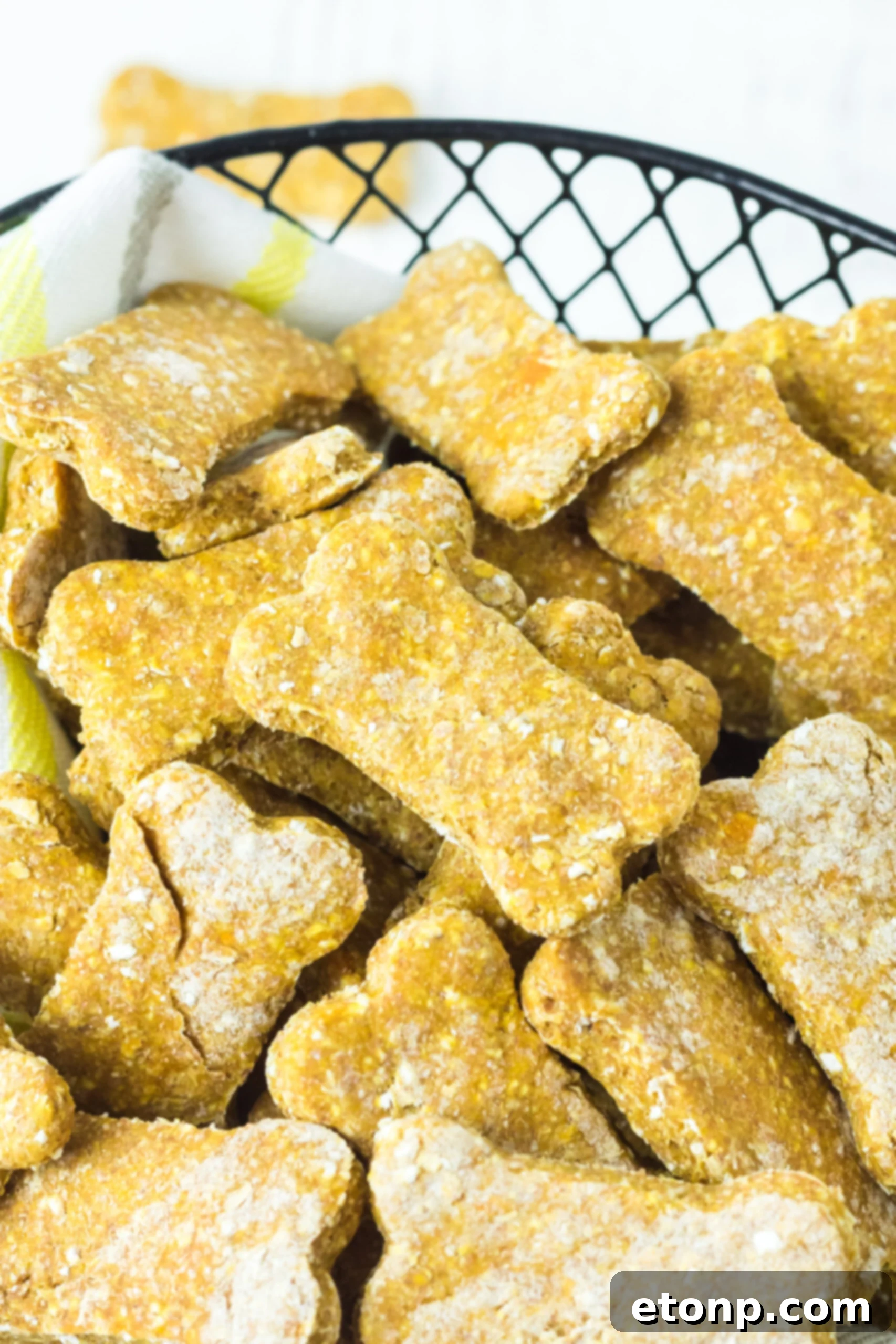 Close up view of healthy homemade Sweet Potato and Pumpkin Dog Treats in a rustic wire basket lined with soft linen, showcasing their golden-orange hue and unique shapes.