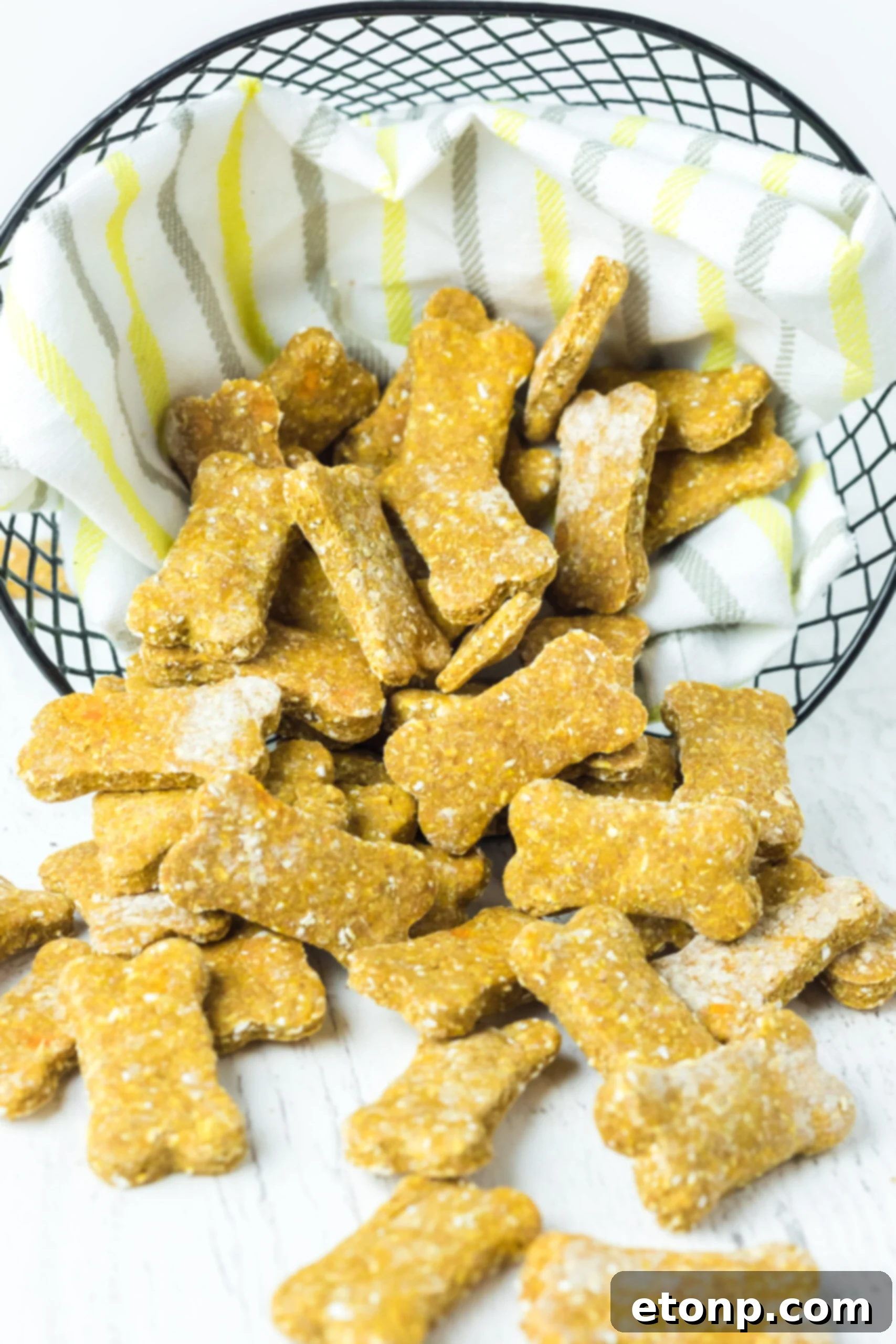 Front view of golden-brown Sweet Potato and Pumpkin Dog Treats playfully spilling out of a wire basket onto a clean linen cloth, highlighting their inviting texture.