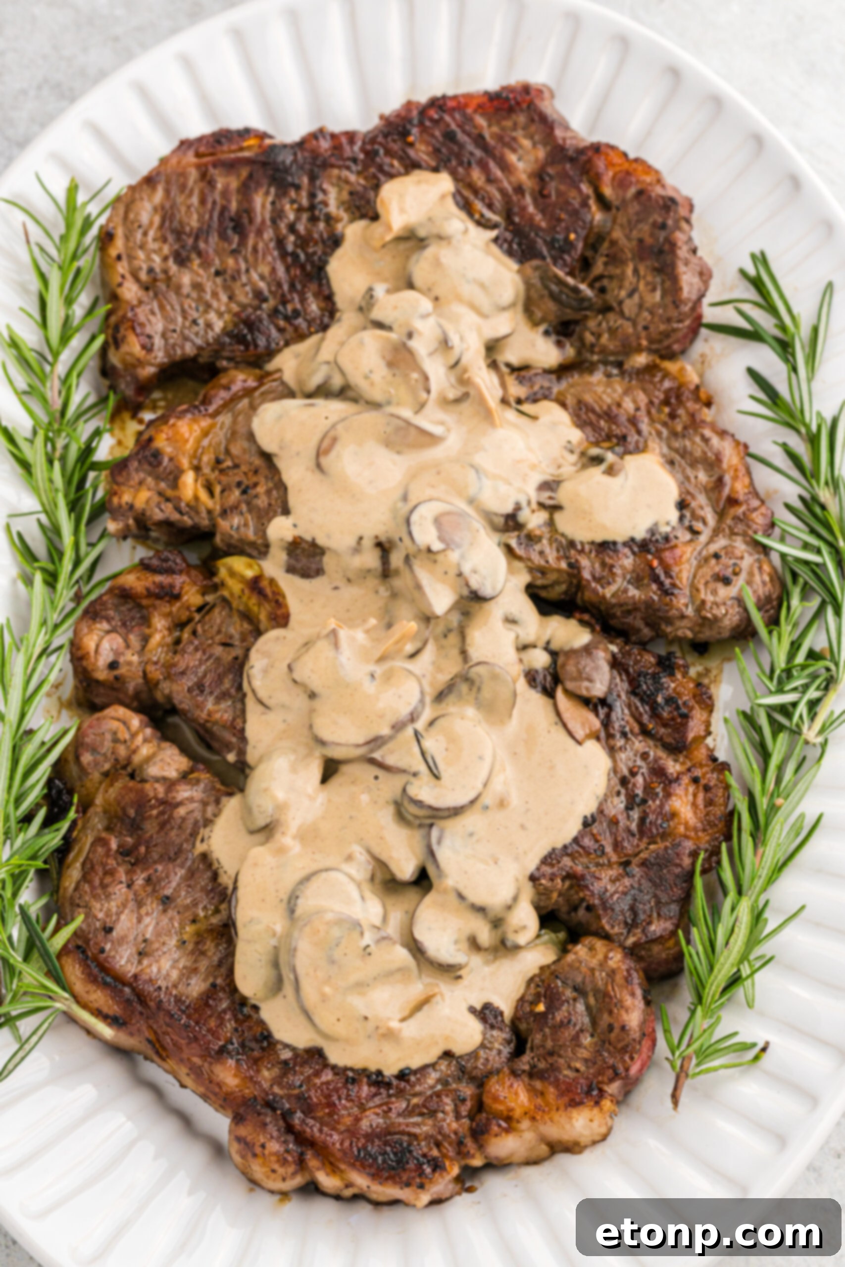 Ultimate Garlic Butter Steak 2 Overhead view of two perfectly seared Garlic Butter Steaks glistening on a white serving dish, garnished with fresh herbs and a rich mushroom sauce.