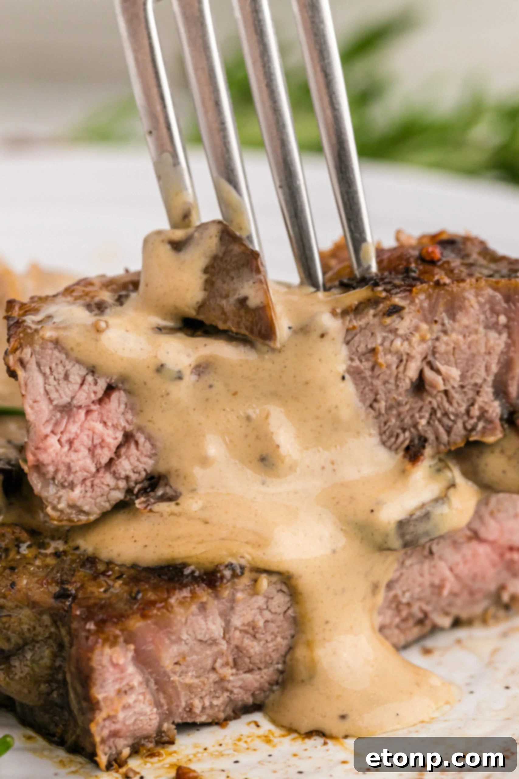 Ultimate Garlic Butter Steak 13 Close-up view of a perfectly cooked Garlic Butter Steak, sliced in half and stacked, with a silver fork digging in, highlighting its tenderness.