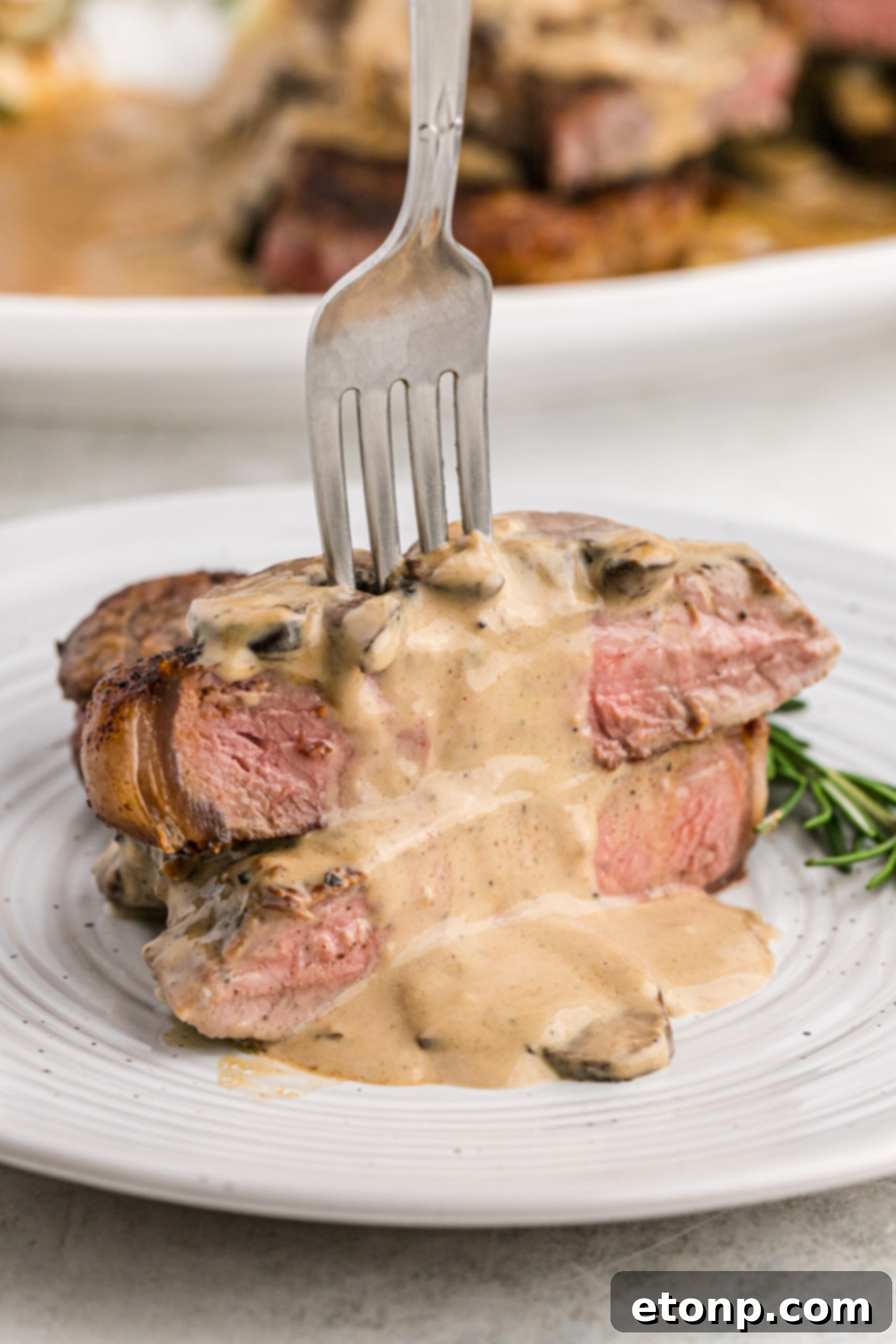 Ultimate Garlic Butter Steak 14 Front view of a beautifully cooked Garlic Butter Steak, cut and stacked on a white plate with a silver fork, showcasing its tender texture.