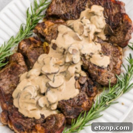 Ultimate Garlic Butter Steak 15 A beautifully seared steak with garlic and herbs, glistening on a white plate, ready to be served.