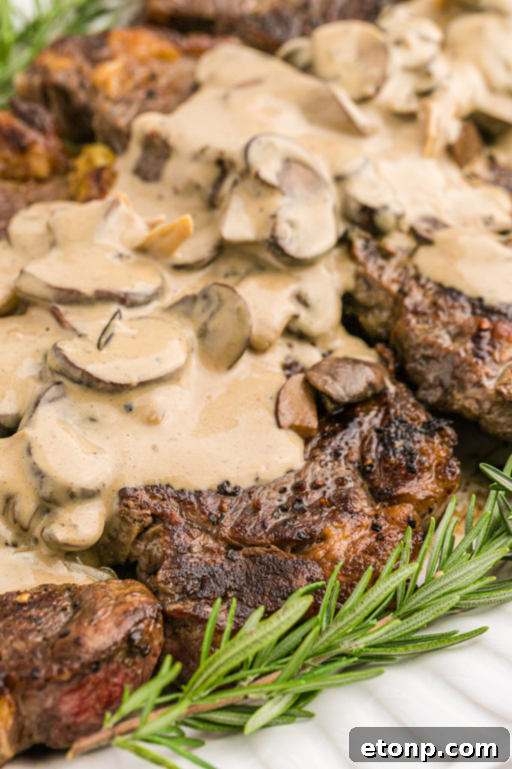 Ultimate Garlic Butter Steak 4 Close-up view of a perfectly cooked Garlic Butter Steak, cut to reveal its juicy interior, garnished with fresh rosemary and roasted garlic cloves.