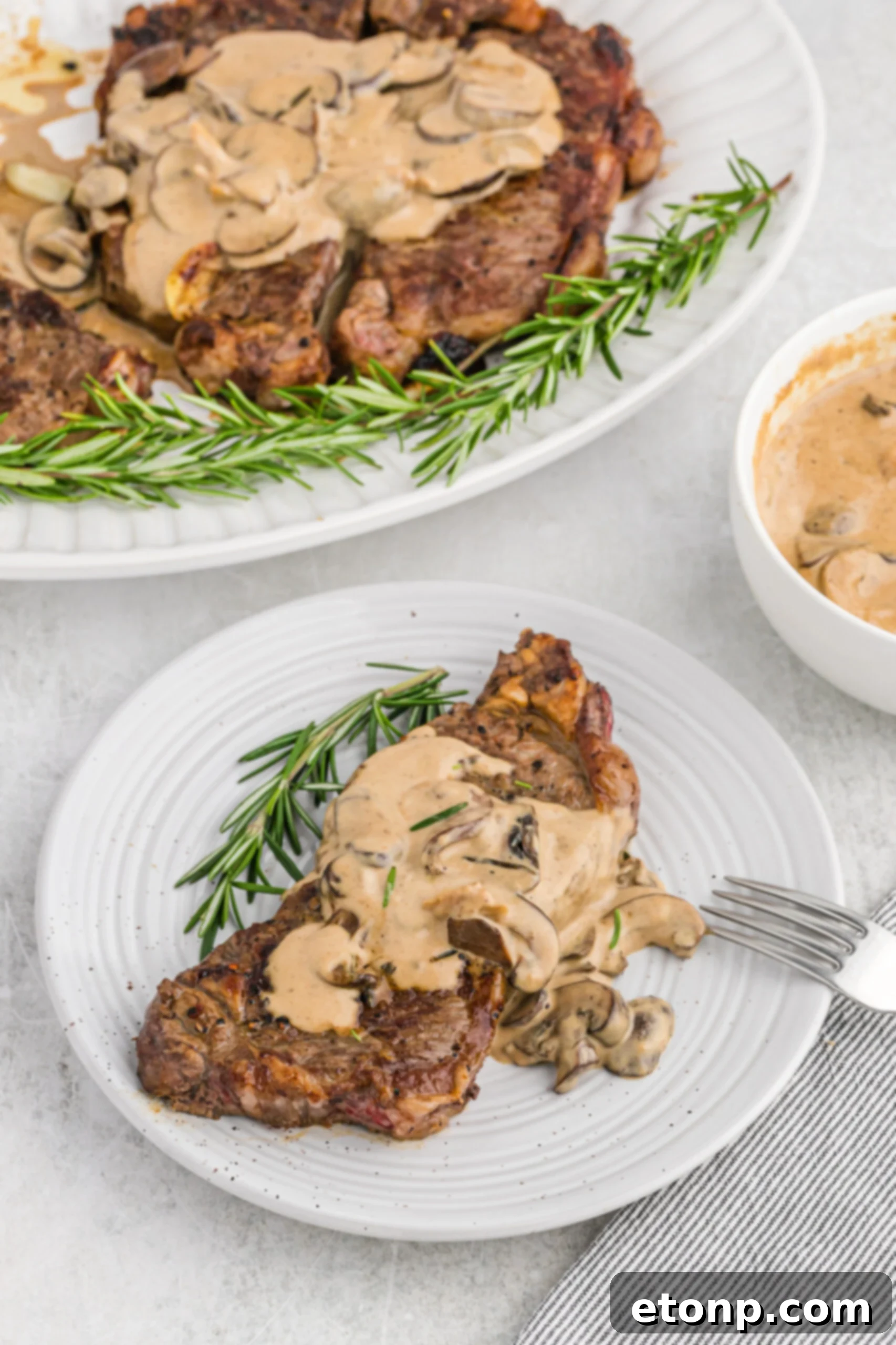 Ultimate Garlic Butter Steak 6 Overhead view of a perfectly cooked Garlic Butter Steak on a pristine white dish, elegantly served with a silver fork, showcasing its readiness.