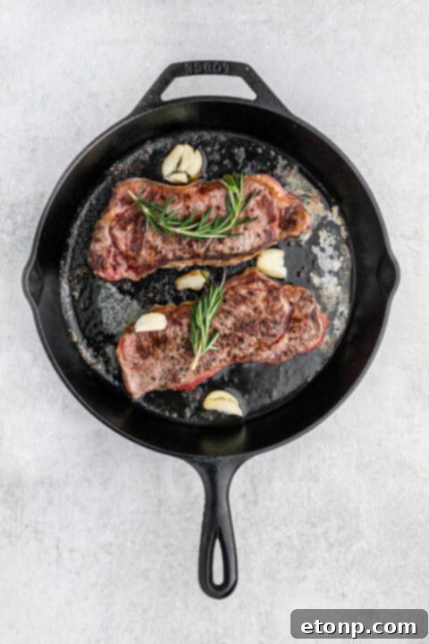 Ultimate Garlic Butter Steak 8 Basting a sizzling steak with garlic butter and rosemary sprigs.