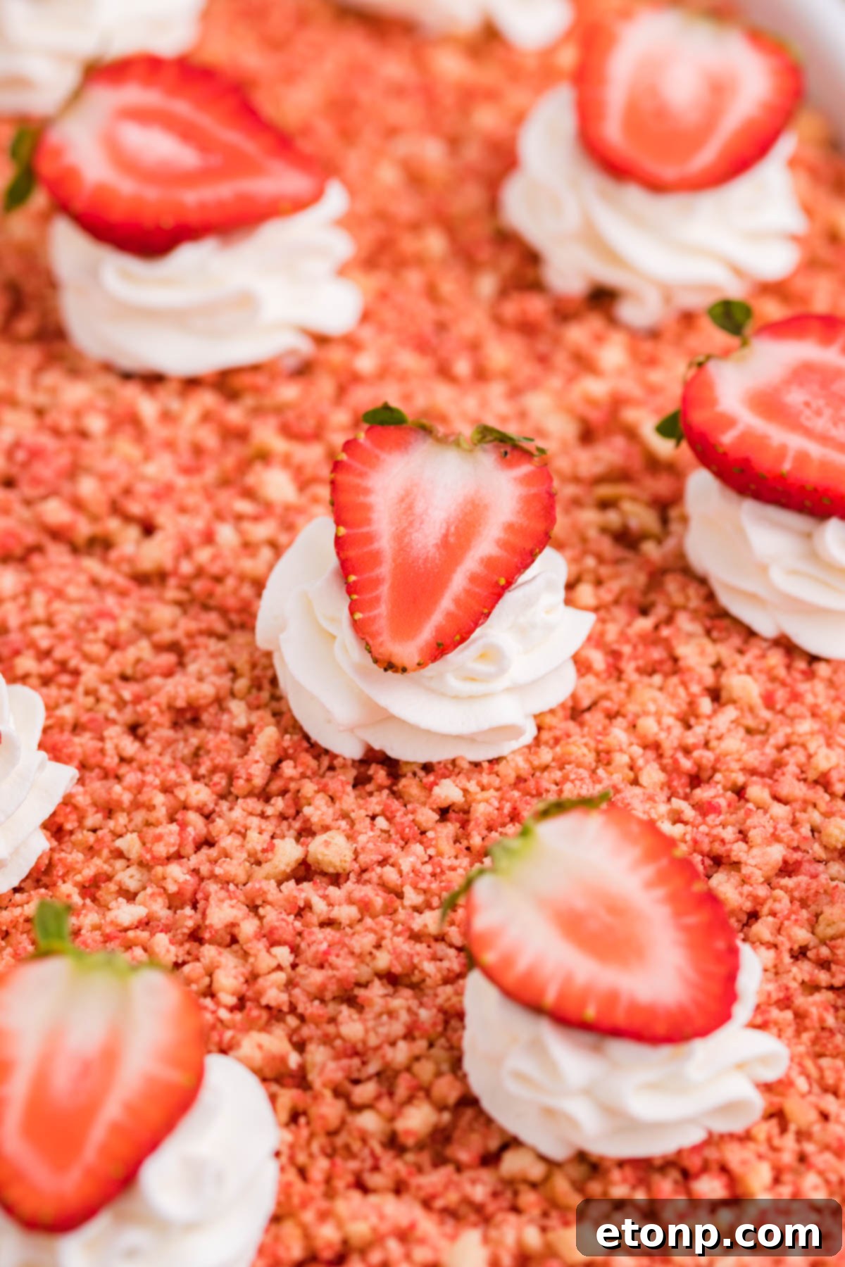 Close up view of Strawberry Crunch Poke Cake in a white baking dish, highlighting the vibrant strawberry color and topping.
