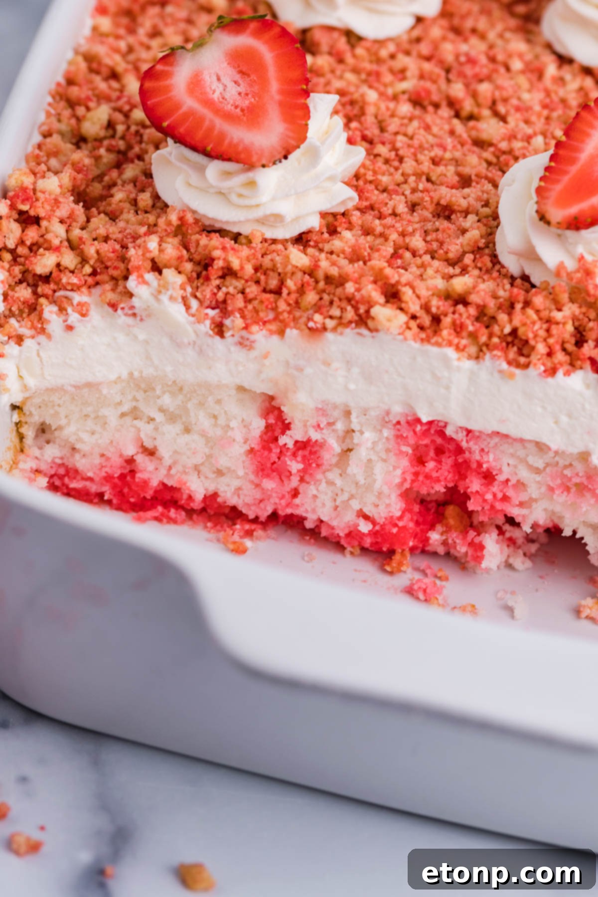 Close up view of Strawberry Crunch Poke Cake in a white baking dish with a slice removed, revealing the moist interior.