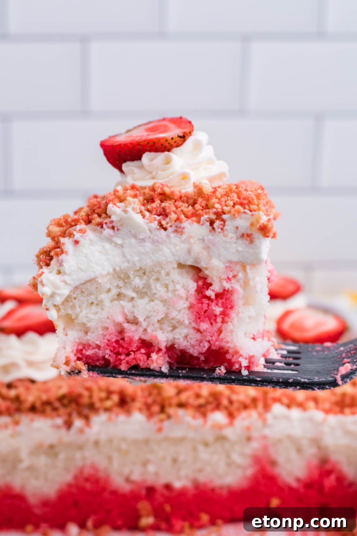 Front view of a bite of Strawberry Crunch Poke Cake on a black fork, showing the distinct layers.