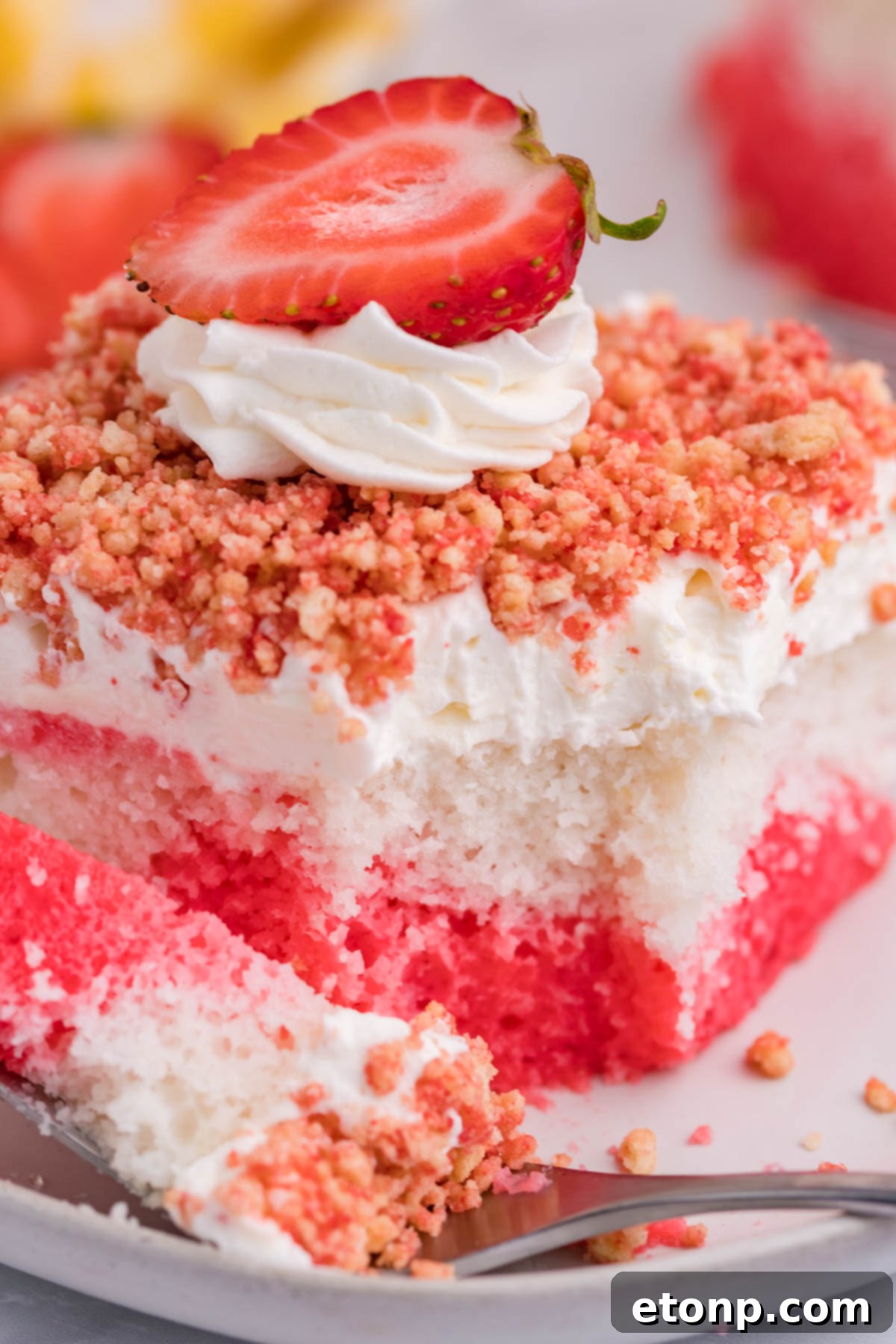 Front view of a piece of Strawberry Crunch Poke Cake with a bite removed by a silver fork, highlighting the soft cake texture.