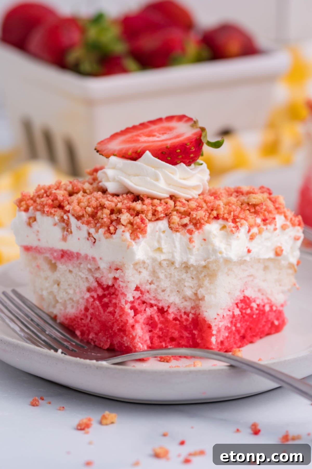 Front view of a piece of Strawberry Crunch Poke Cake with a bite removed by a silver fork, showing its delicious layers.