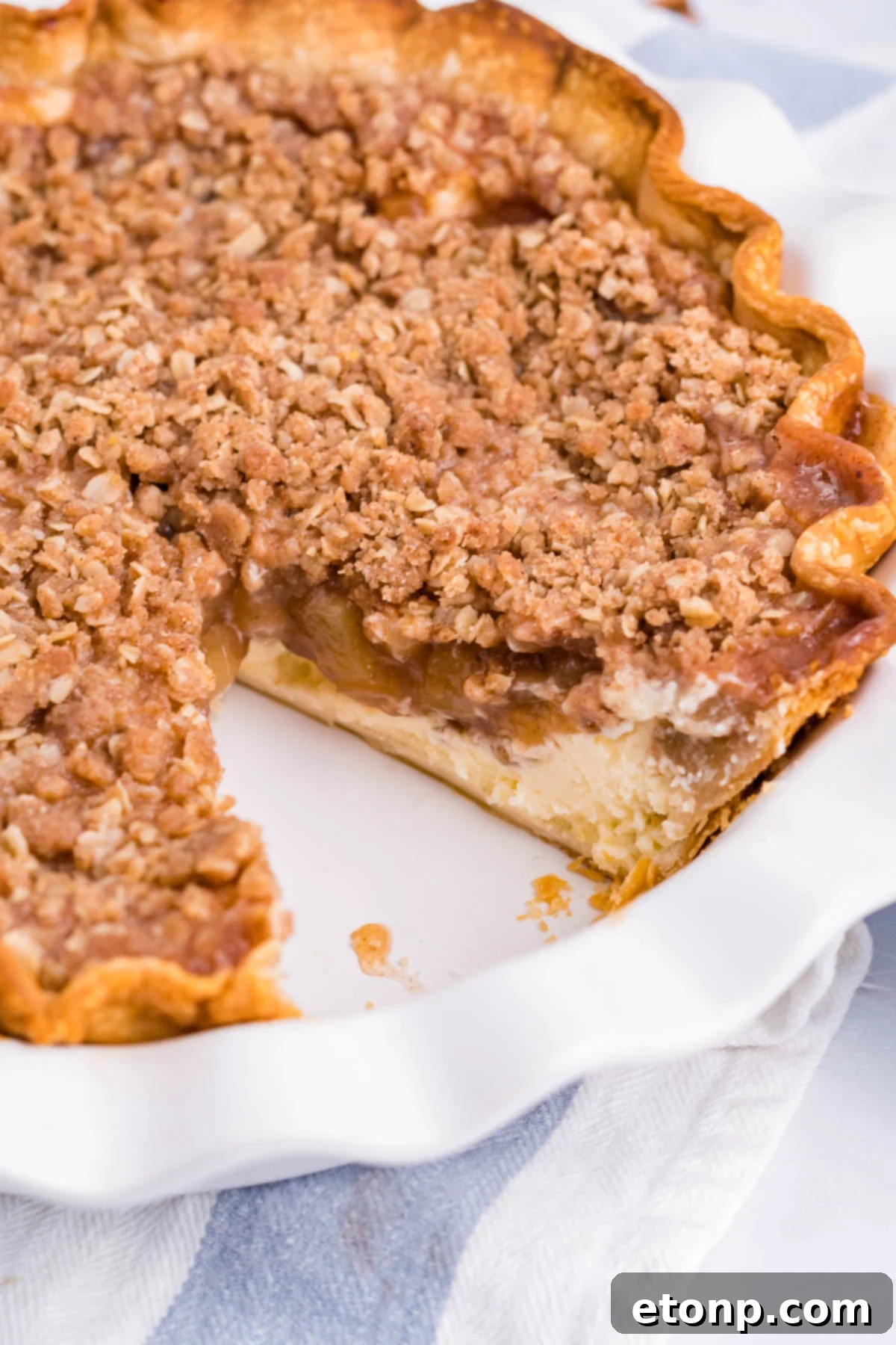 Close up view of Apple Crumb Cheesecake Pie in a white pie dish with a slice removed.