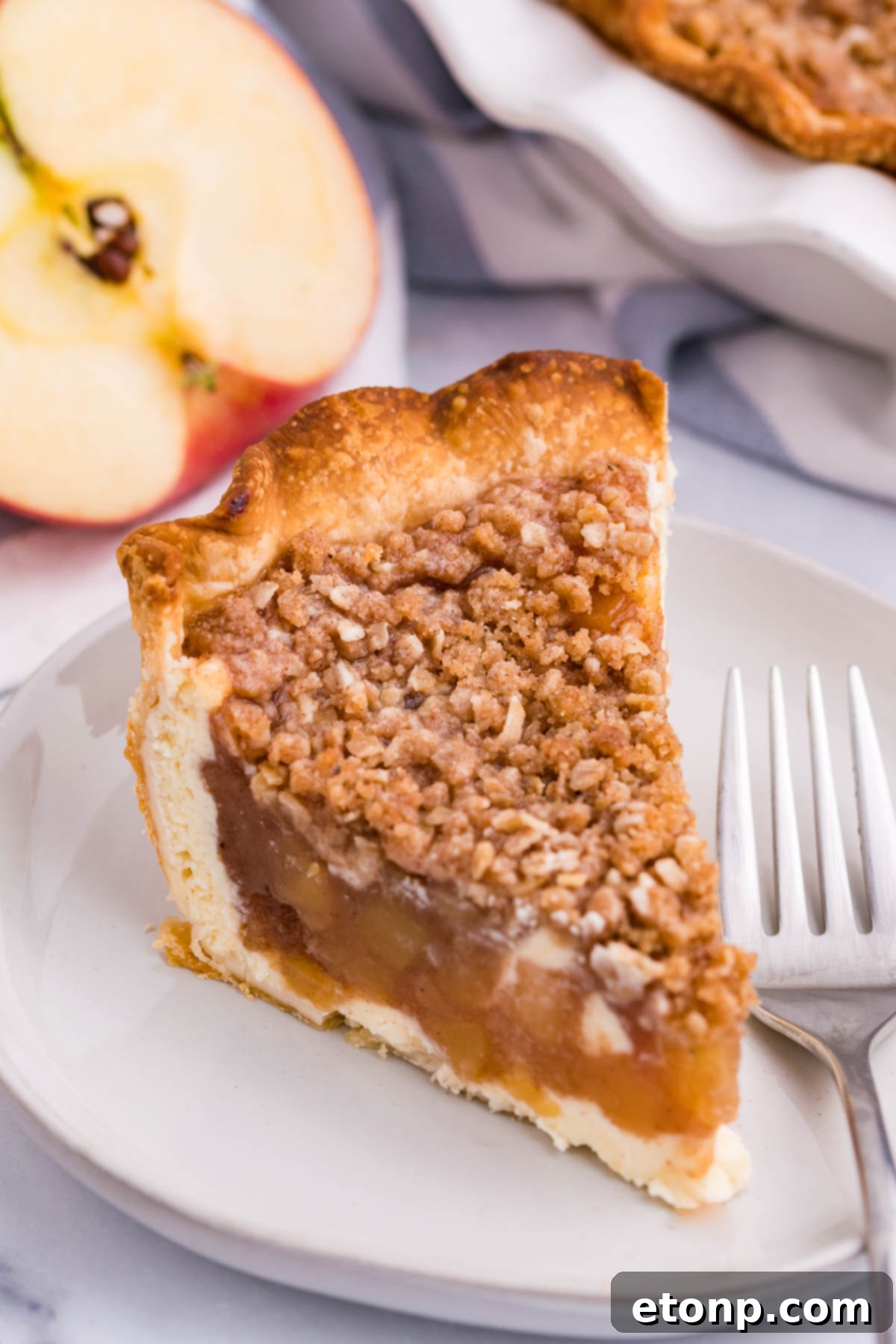 Close up view of a slice of Apple Crumb Cheesecake Pie on a white dish.