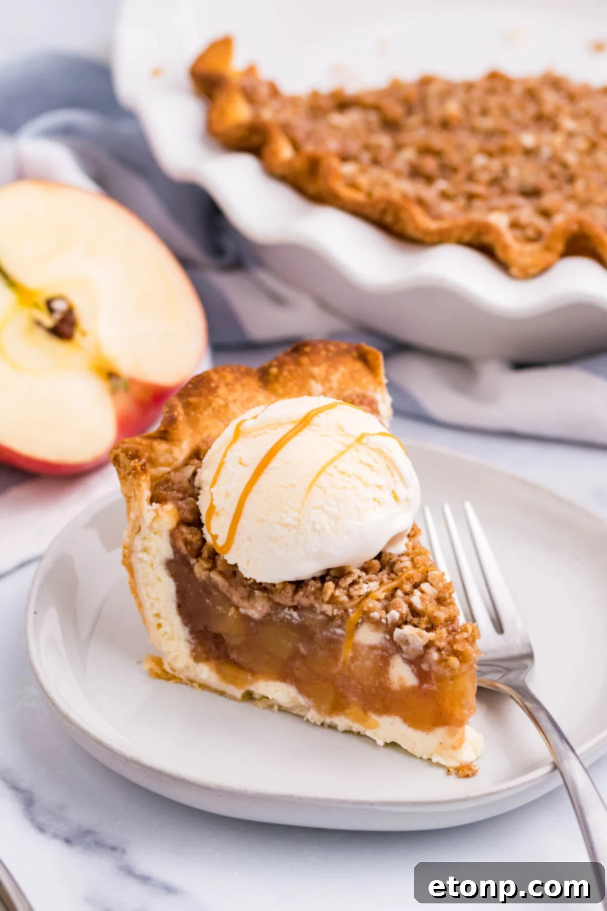 Front view of a slice of Apple Crumb Cheesecake Pie on a white dish with a scoop of vanilla ice cream.