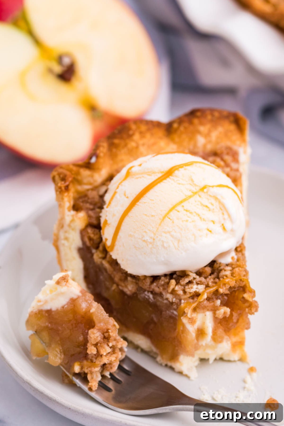 Front view of a slice of Apple Crumb Cheesecake Pie on a white dish with a scoop of vanilla ice cream with a bite removed by a silver fork.
