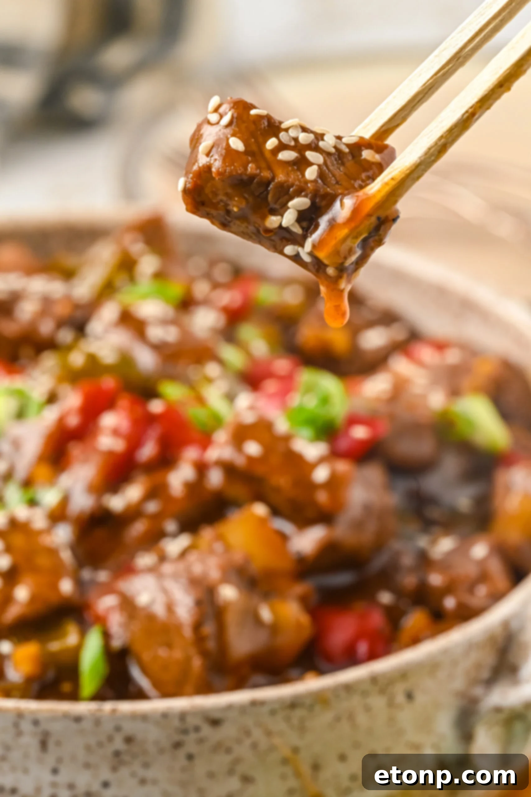 Close up view of chopsticks holding a piece of Chinese Pepper Steak.