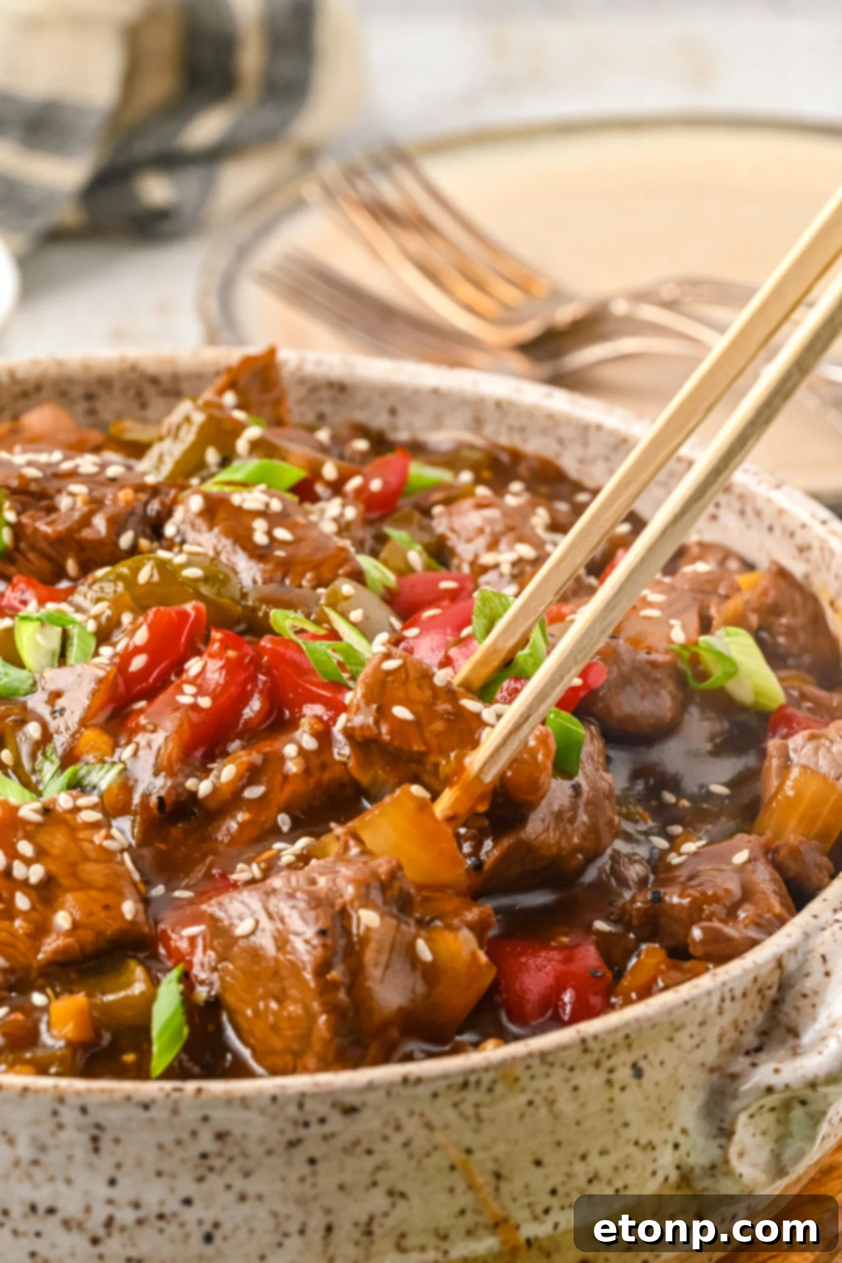 Close up view of chopsticks holding a piece of Chinese Pepper Steak.