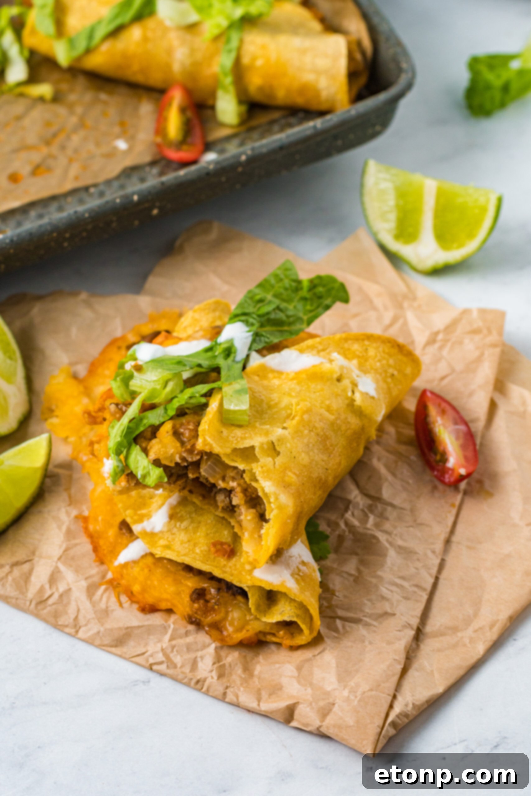 Front view of two Crispy Baked Beef Tacos stacked on parchment paper, with a bite removed from the top taco revealing the succulent filling.
