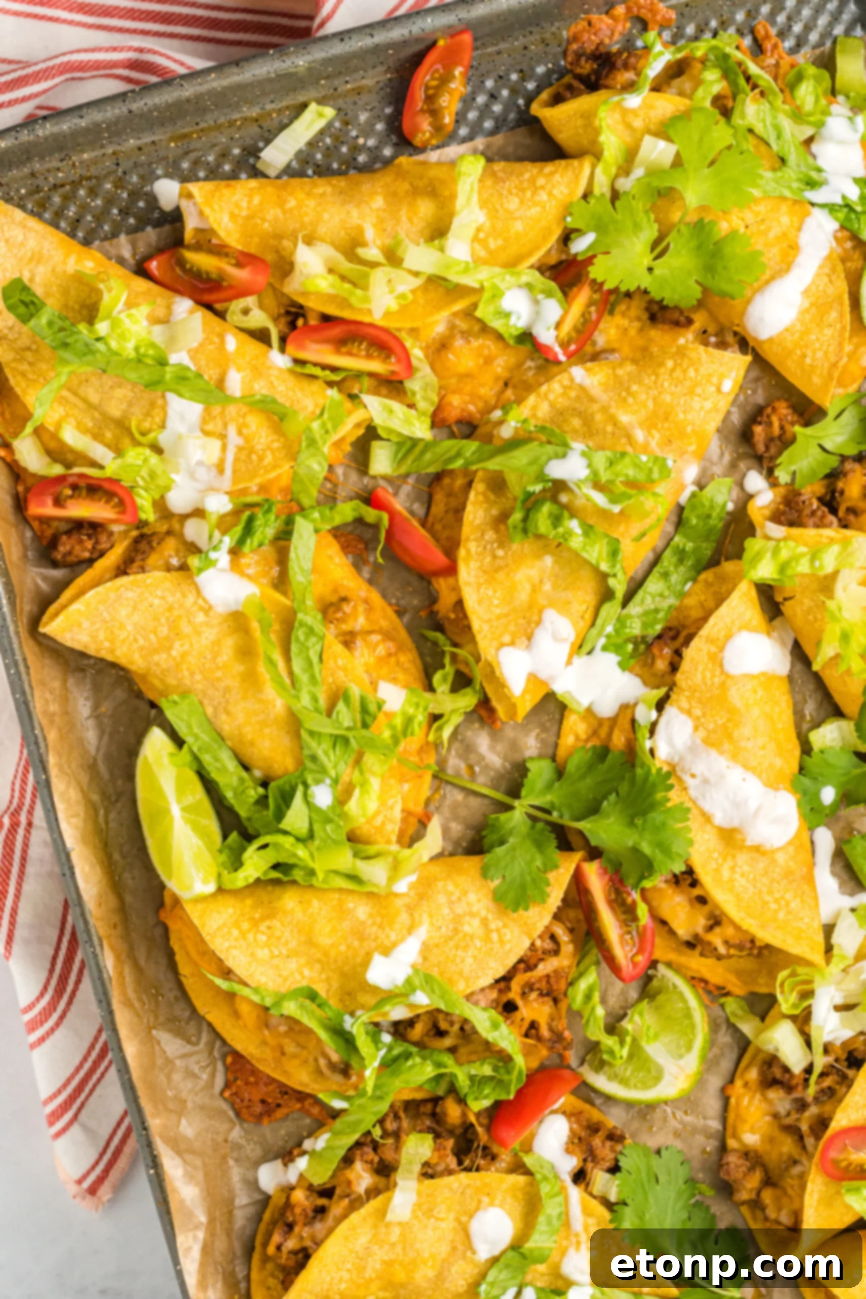 A second overhead view of Crispy Baked Beef Tacos on a sheet pan, showcasing their golden-brown tortillas and ample filling.