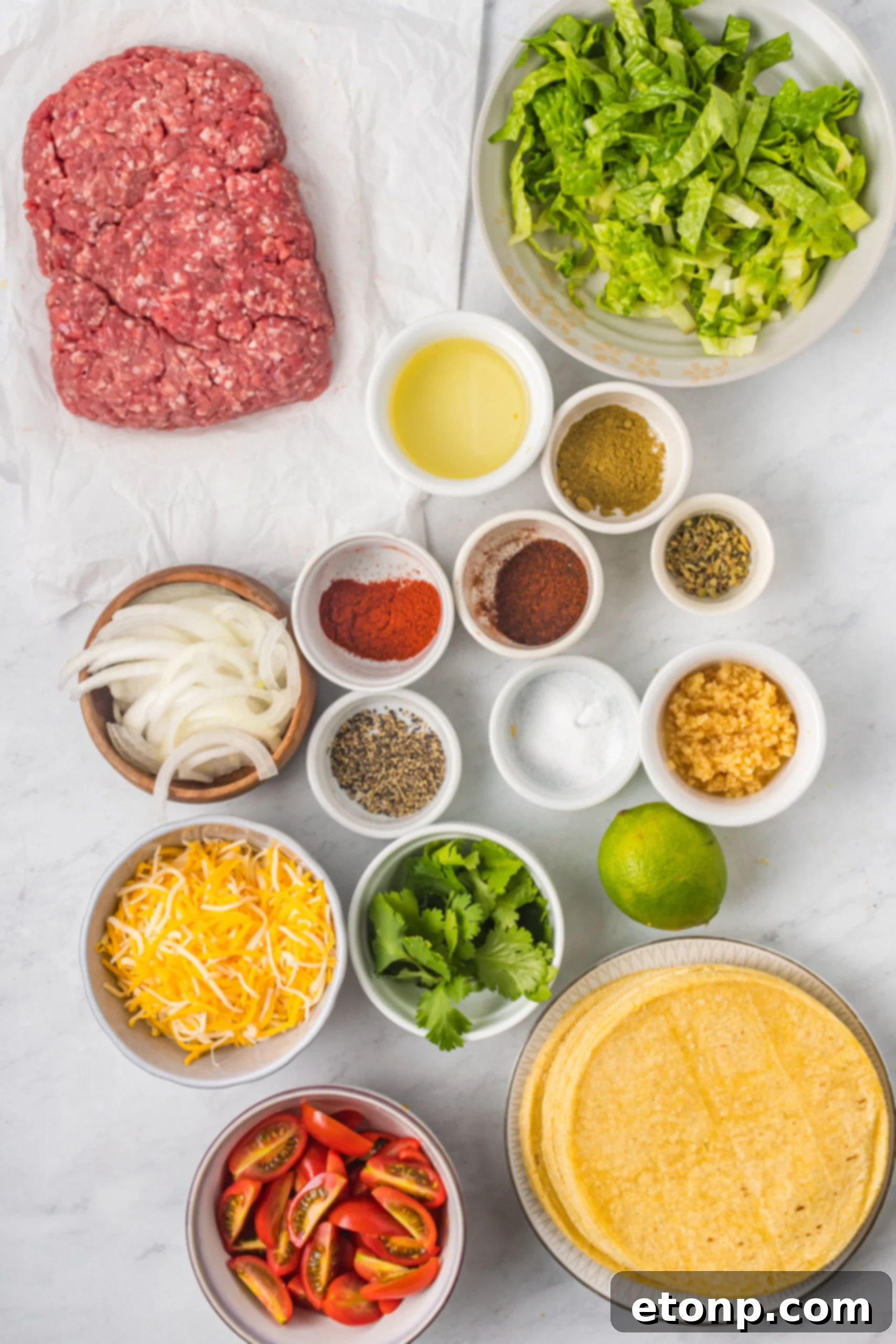 A flat lay photograph displaying all the fresh ingredients required to make the crispy beef taco recipe, including ground beef, spices, vegetables, and tortillas.
