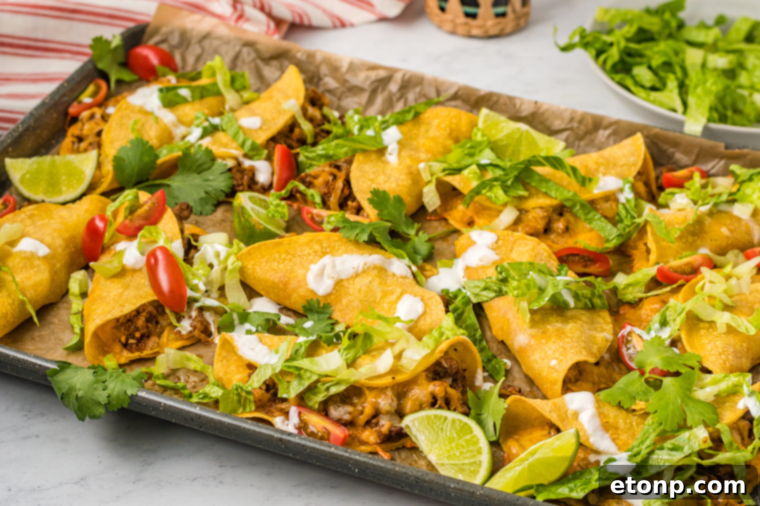 Front view of several Crispy Baked Beef Tacos on a sheet pan, with a rustic tablecloth background, emphasizing their homemade appeal.