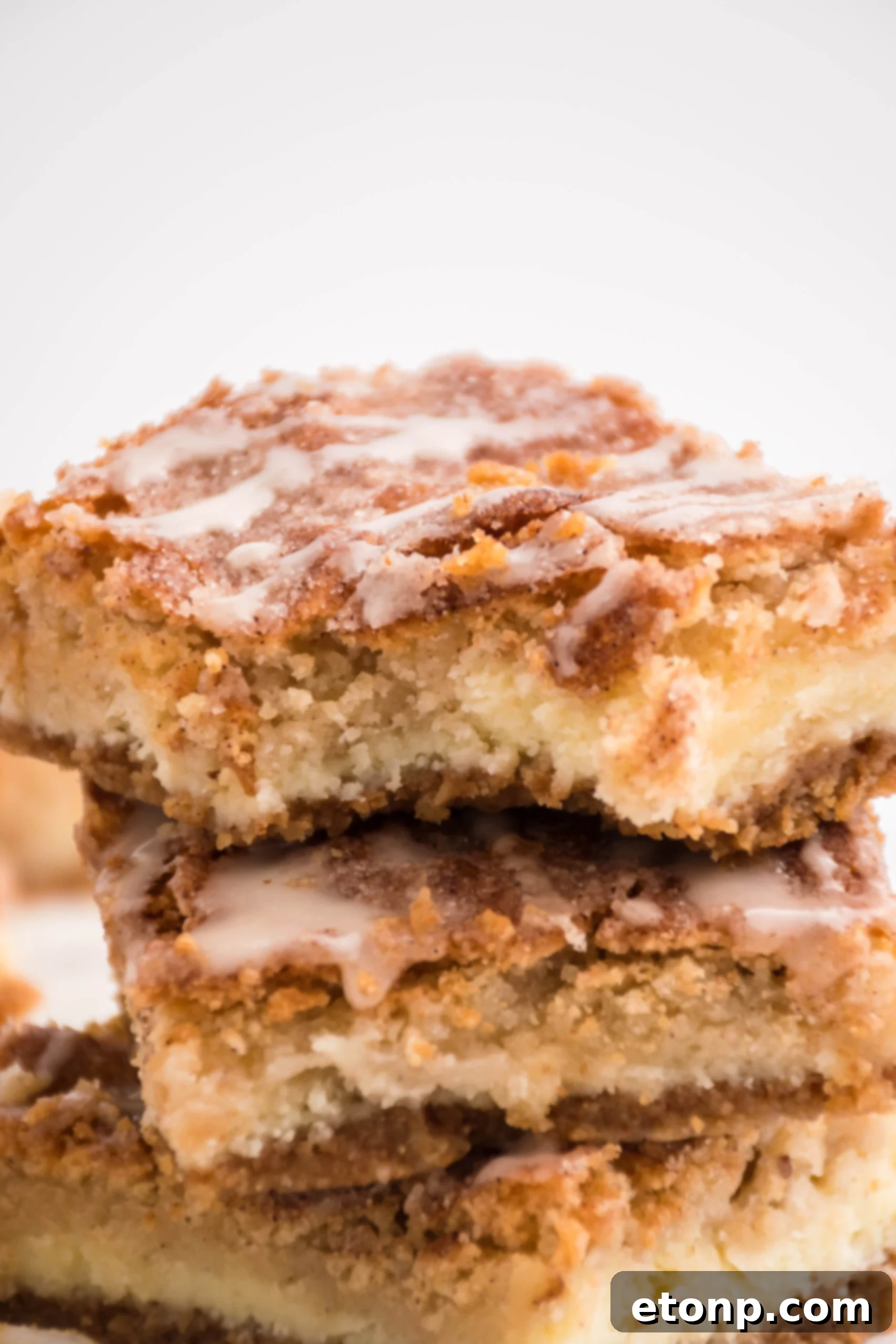 Front view of three Snickerdoodle Cheesecake Bars stacked with a bite removed from the top bar.