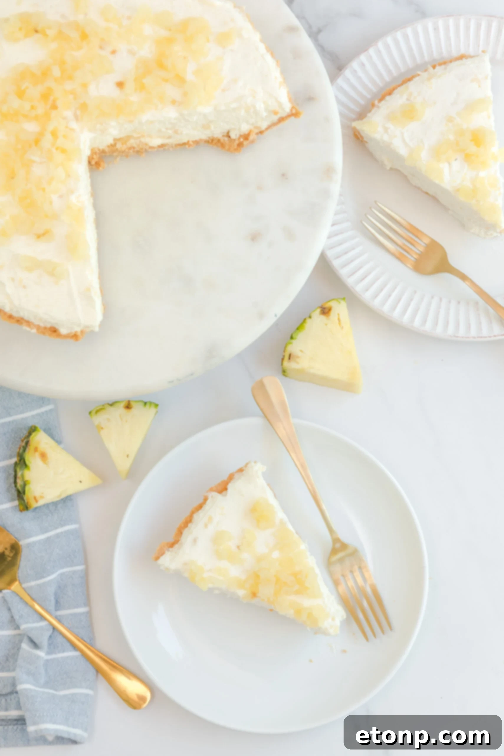Chilled Pineapple Cheesecake Bliss 16 Overhead view of No Bake Pineapple Cheesecake with two slices removed and served on a white plate with gold forks.