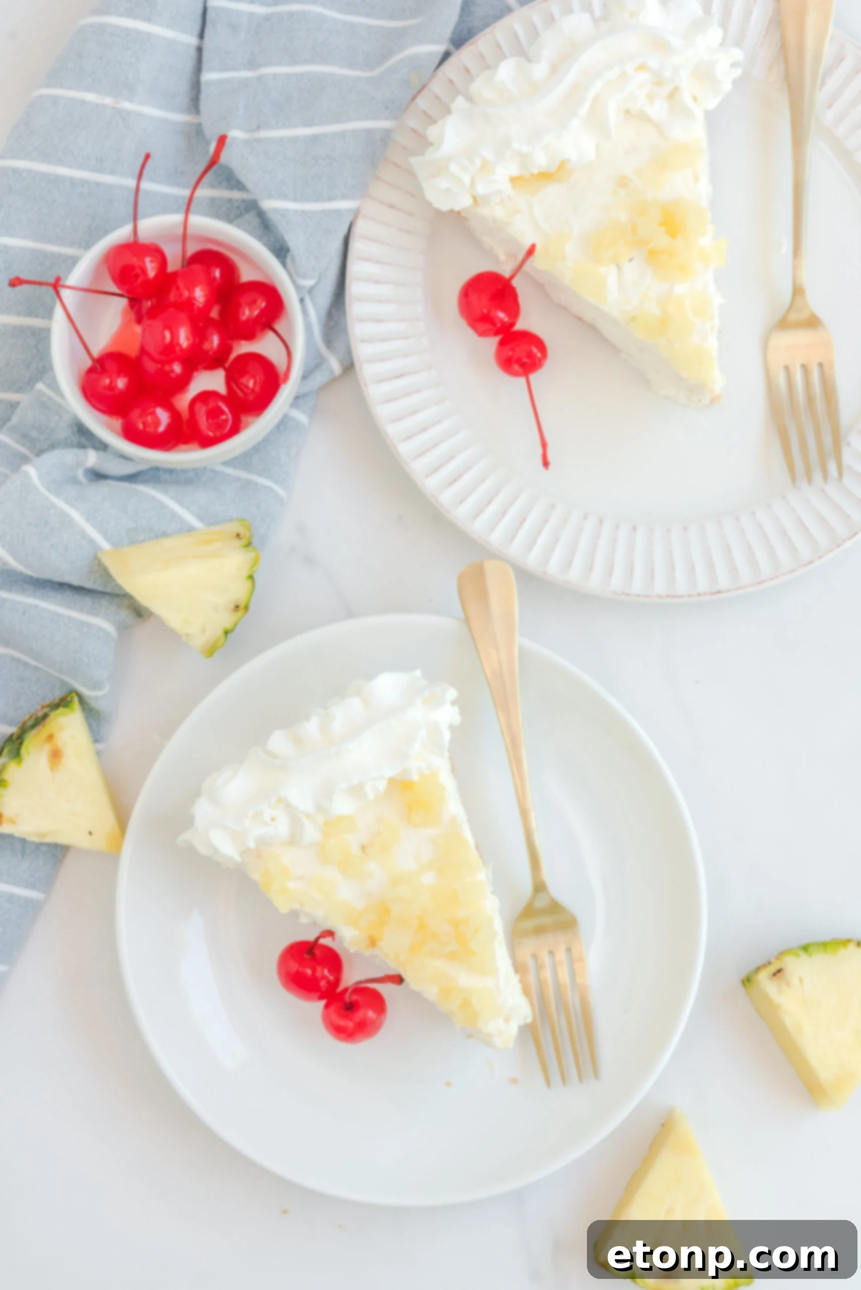 Chilled Pineapple Cheesecake Bliss 18 Overhead view of two slices of No Bake Pineapple Cheesecake served on white plates with gold forks.