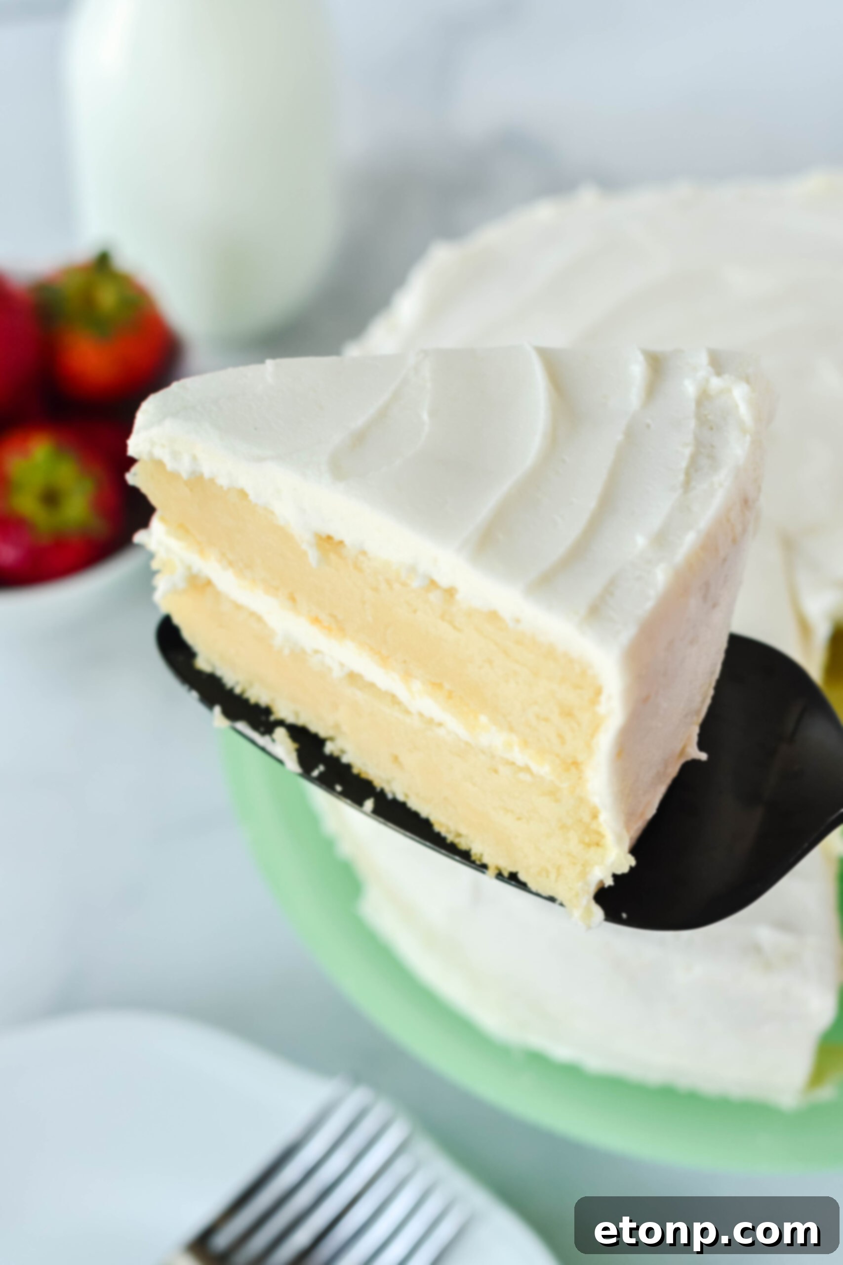 Side view of a generous slice of Classic Vanilla Cake served on a sophisticated black cake server.